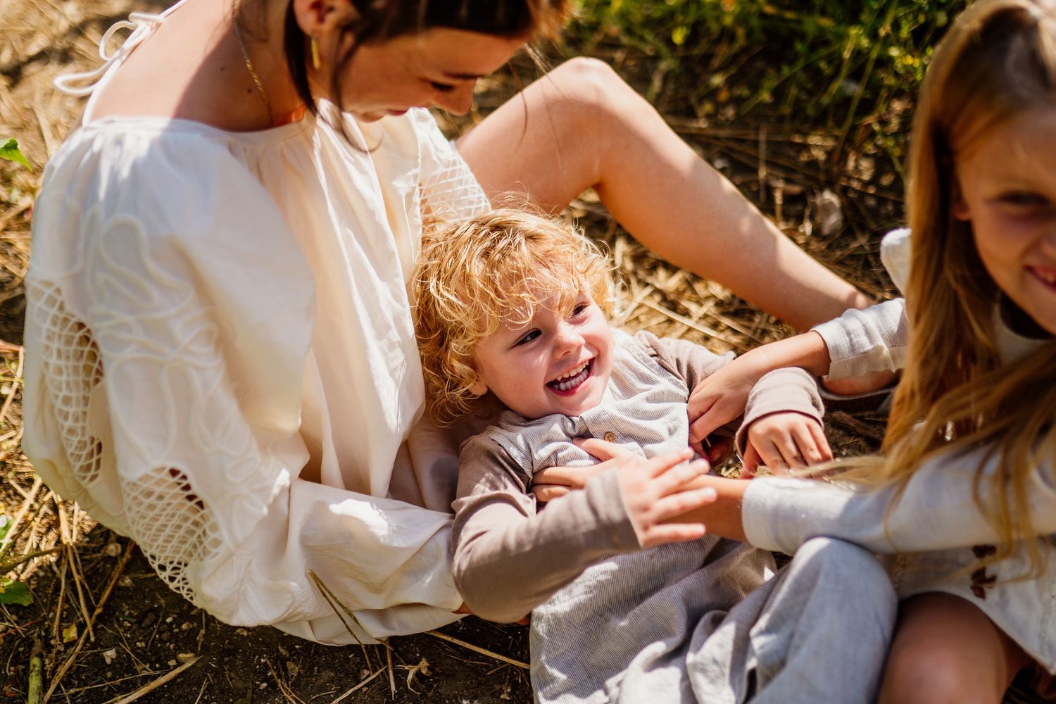 Intimate family cuddles on white blanket in natural sunlight.