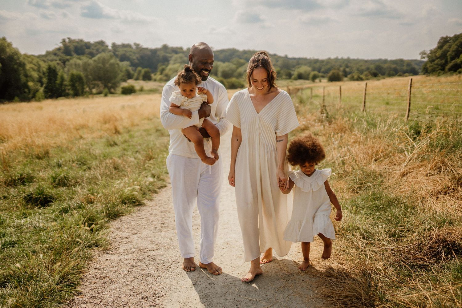 Family walking together on dirt path through sunny summer meadow.