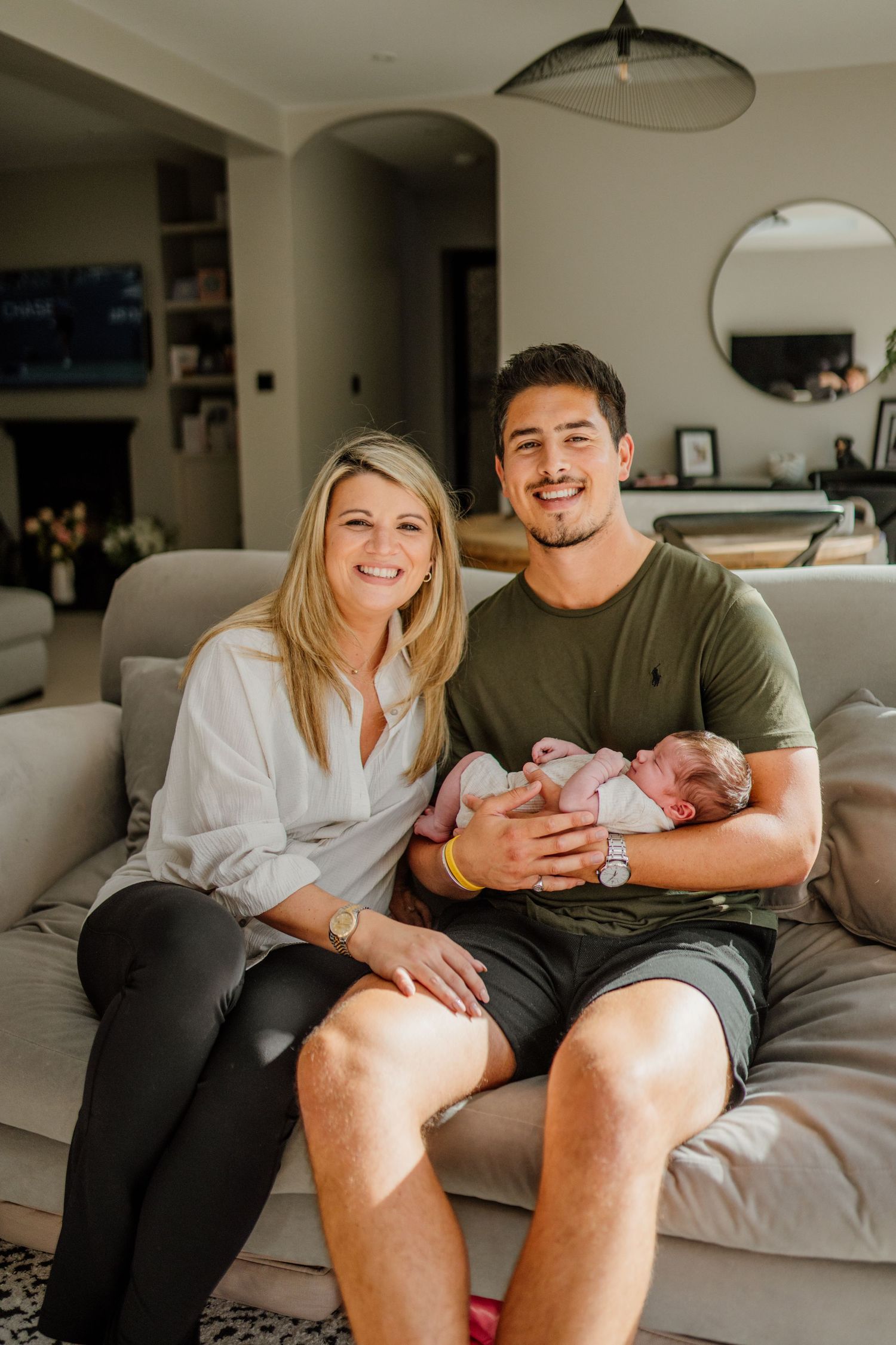 Family relaxing together on grey couch during newborn photo session at home.