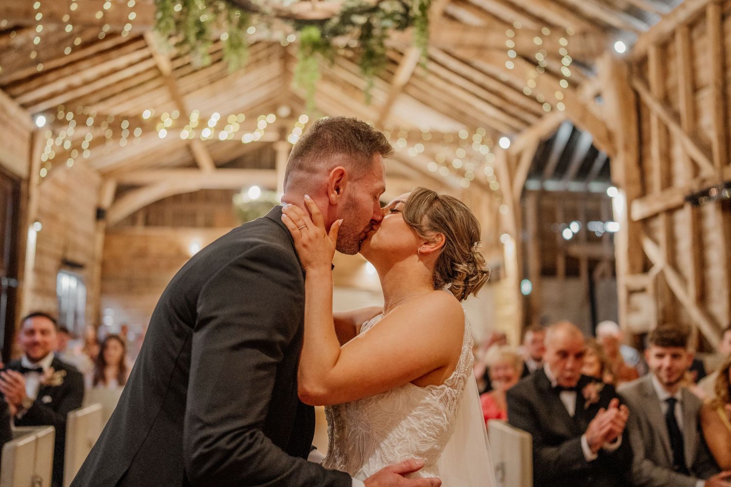 Romantic wedding ceremony in a barn venue with string lights and wooden architecture.
