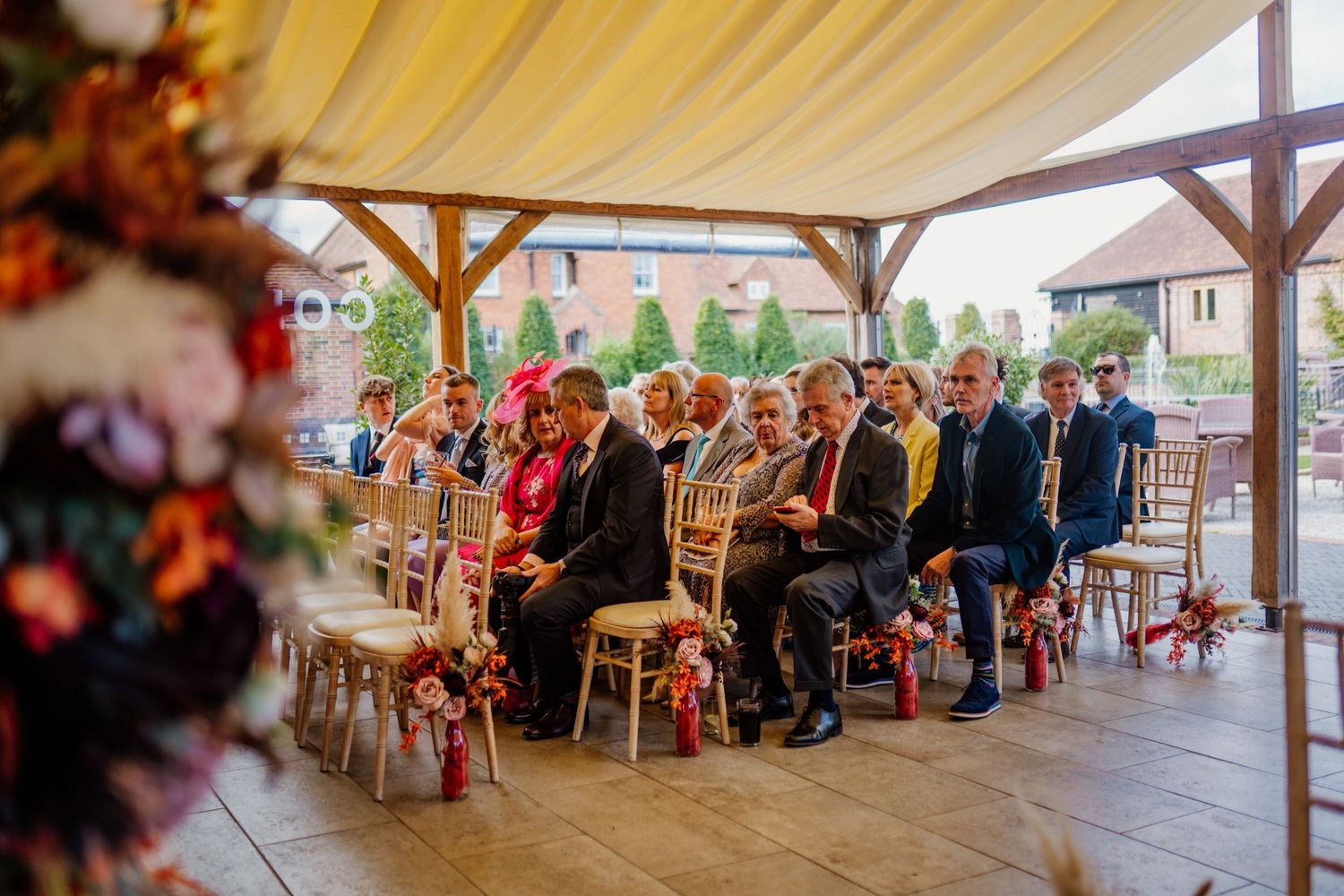 Wedding guests seated under an elegant white tent canopy during an outdoor ceremony celebration.