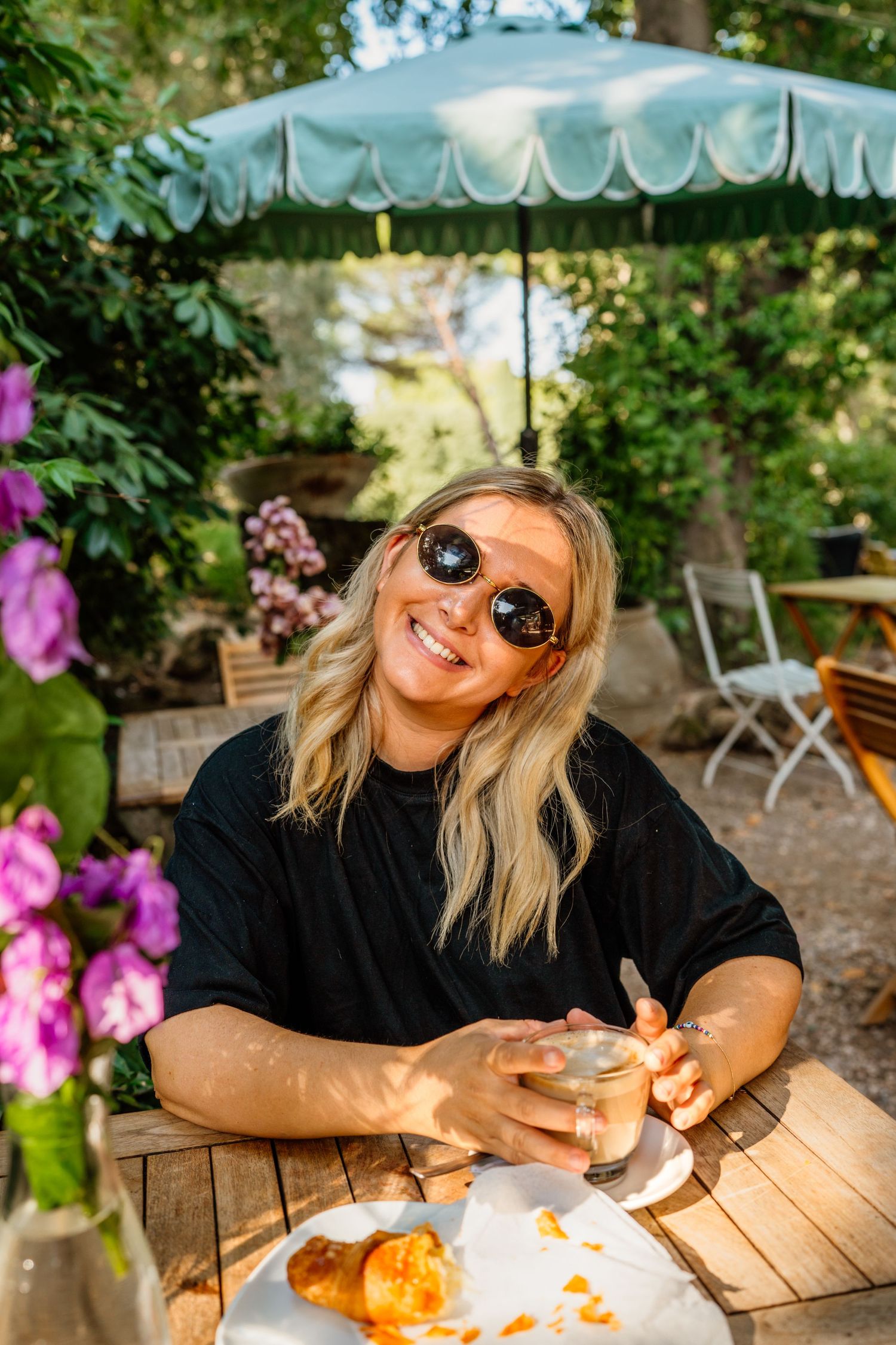 Person enjoying food at outdoor cafe with purple flowers in background.
