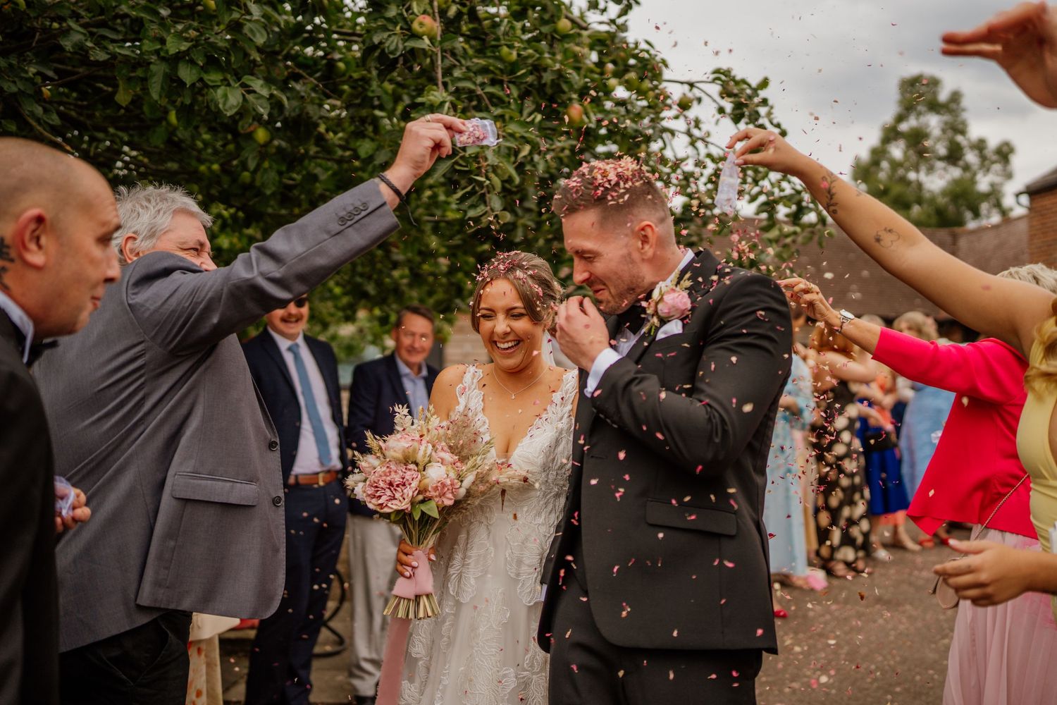 Wedding party celebrating with confetti outdoors on a sunny day.