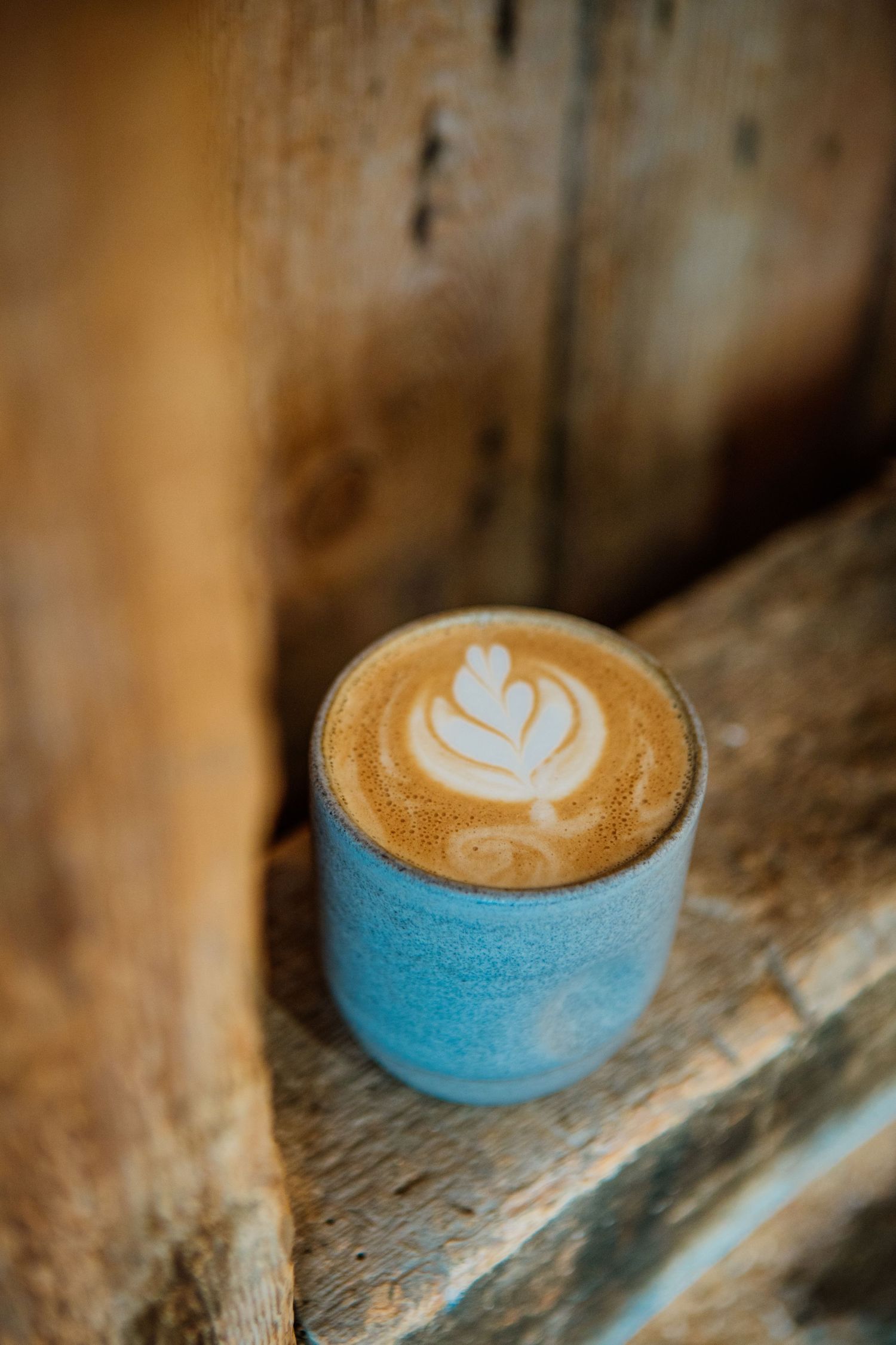 A turquoise ceramic cup filled with latte art featuring a delicate tulip design sits on a rustic wooden surface.