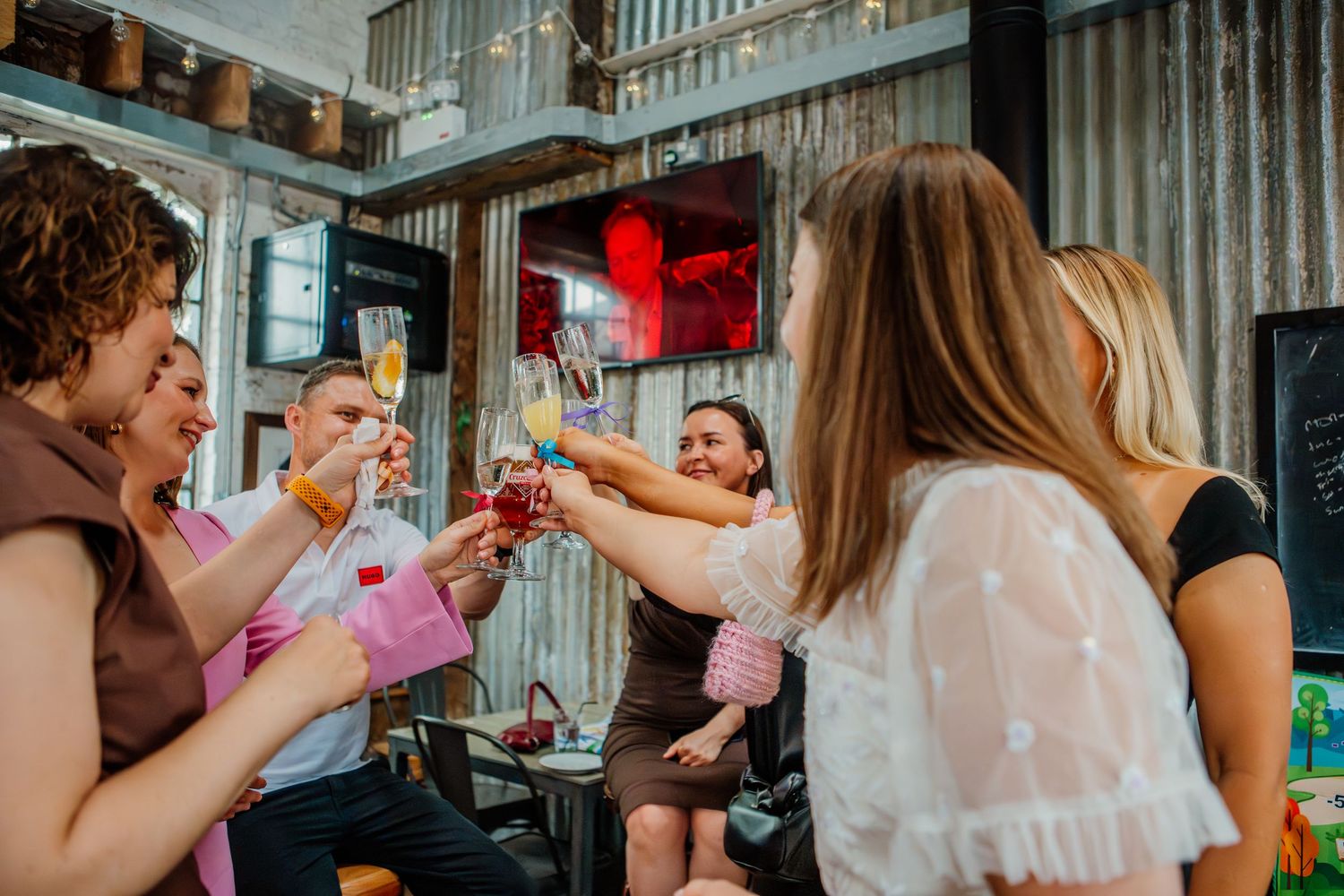 A group of people enjoying a celebratory toast with pink drinks at an indoor party venue.