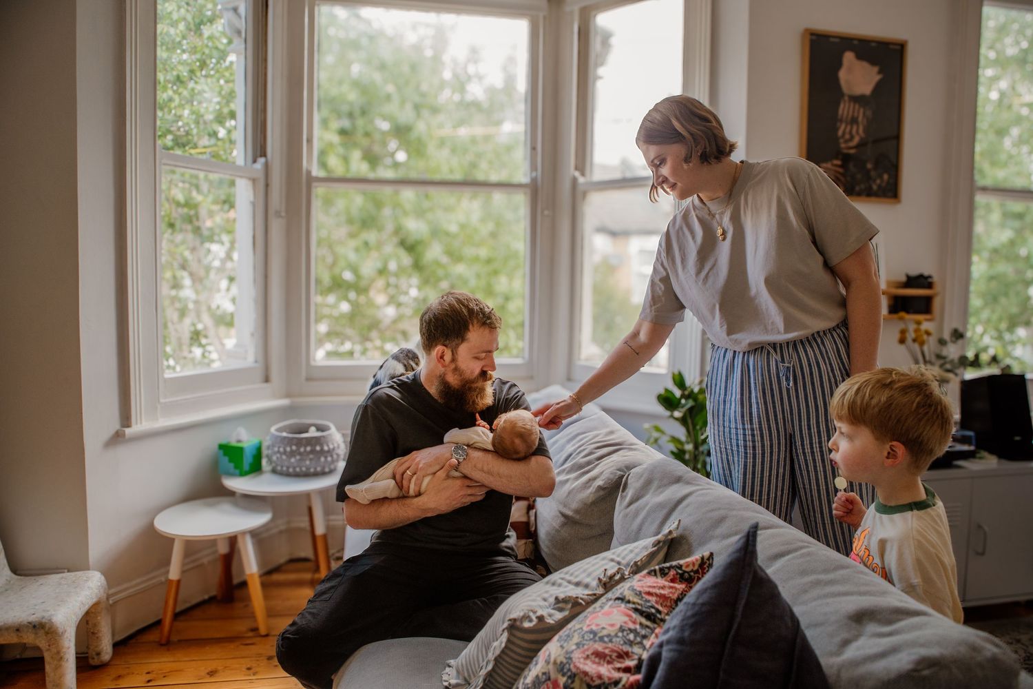 Bright sunlit room with large windows showing casual family interactions.