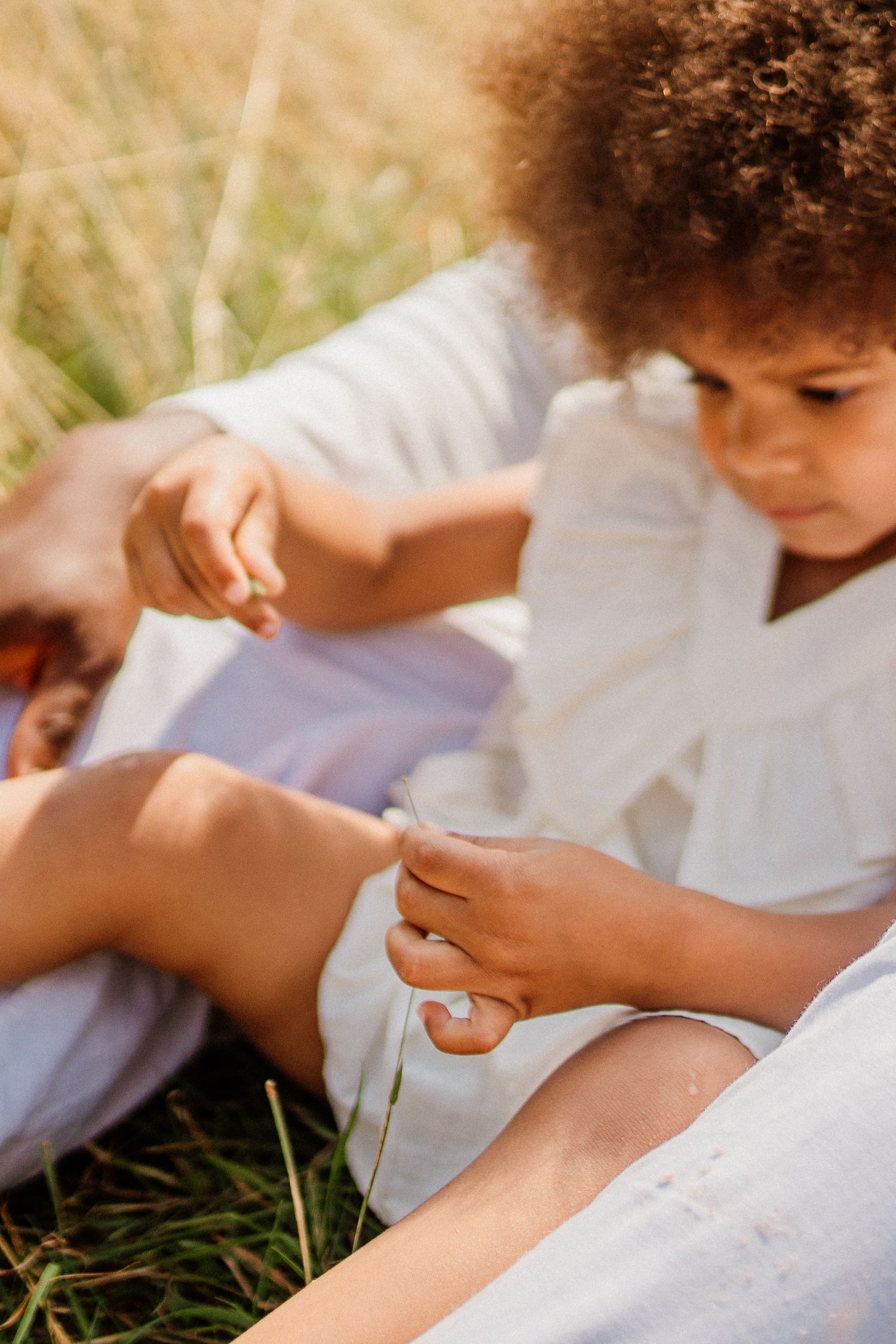 Close-up view of small hands playing in grass while wearing white summer dress.
