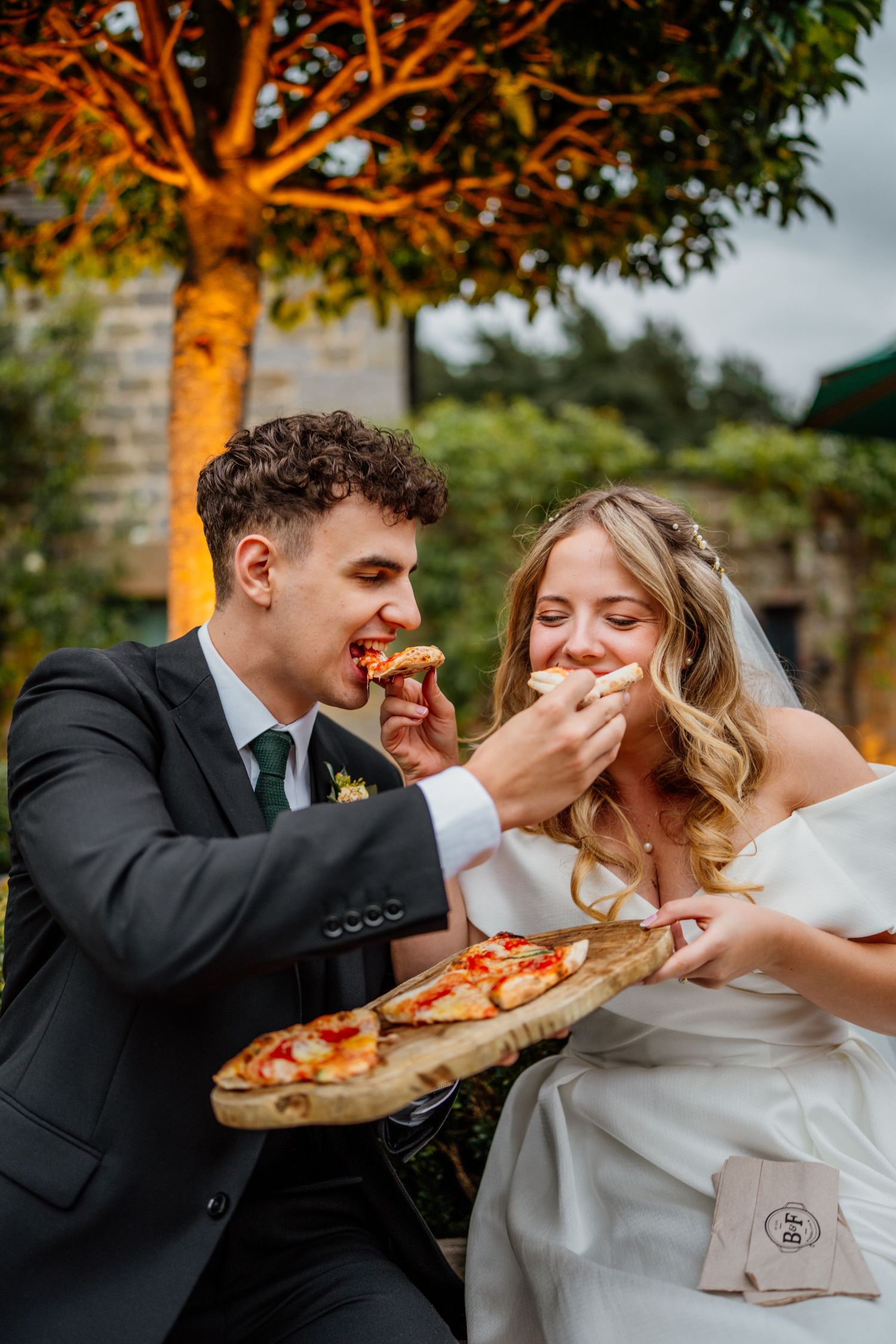 Couple sharing a playful moment eating pizza together at their wedding reception.