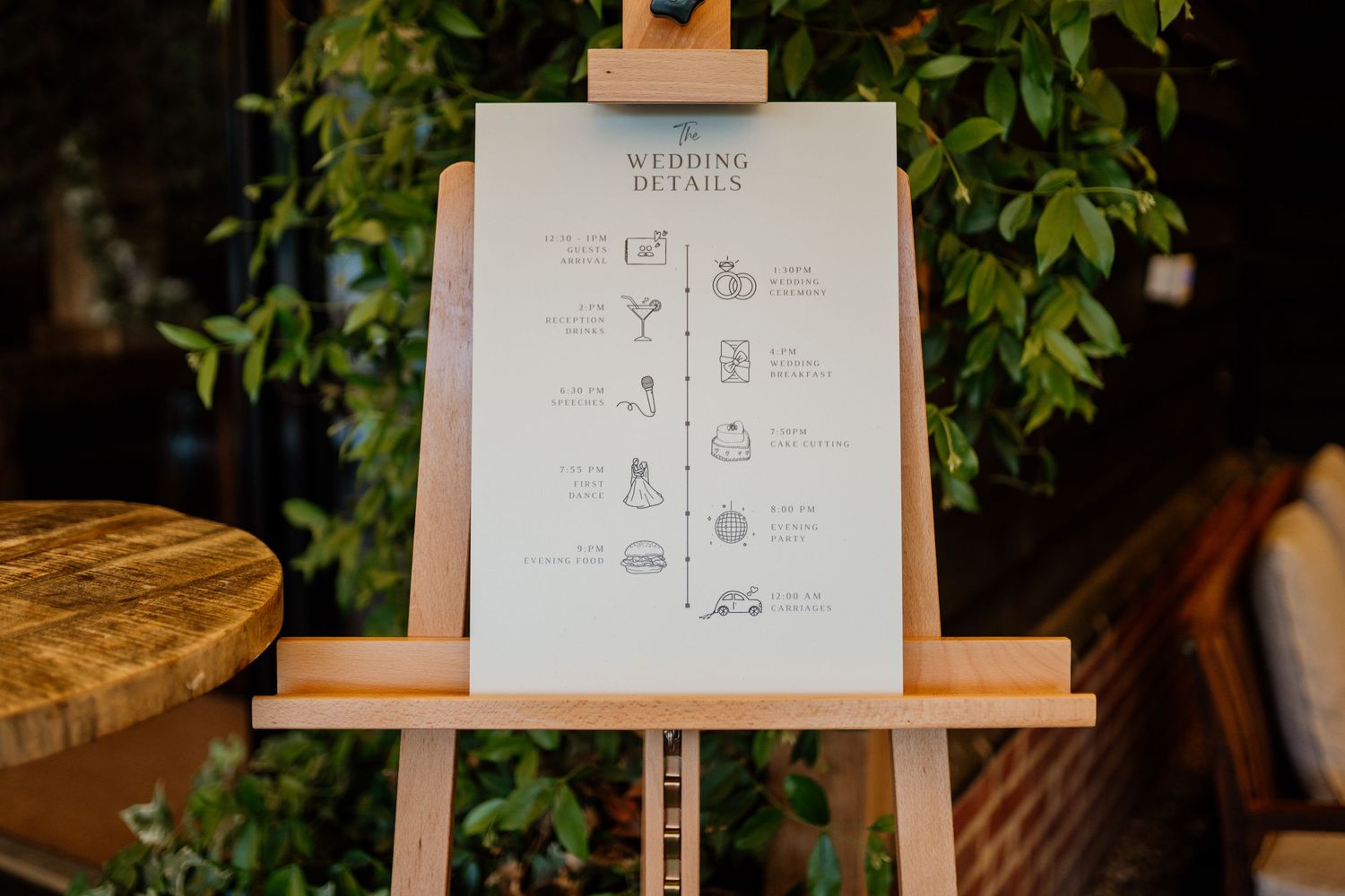 Wedding details displayed on elegant signage with floral decor and wooden easels at an outdoor reception venue.