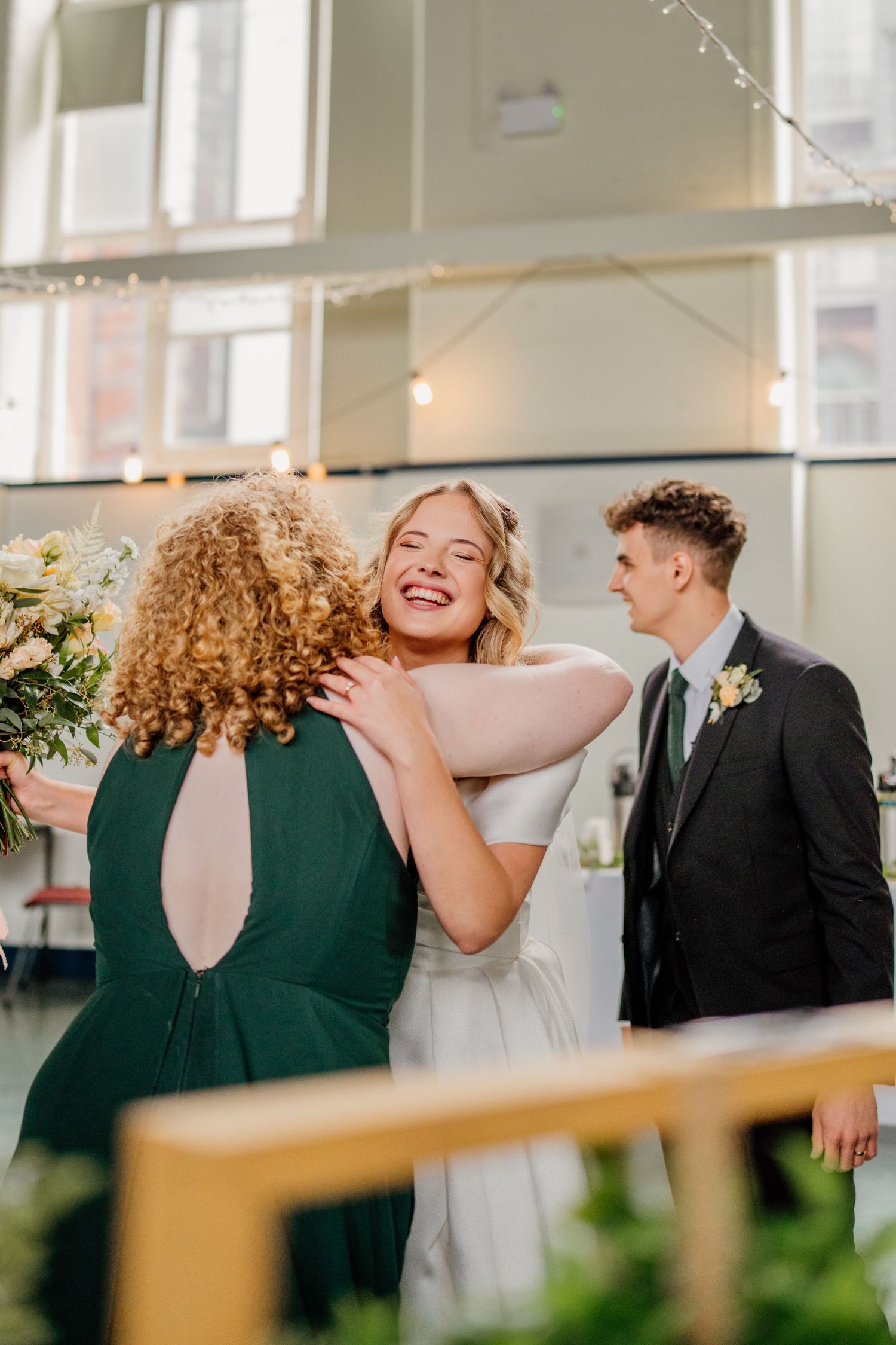 Candid wedding party moment with bridesmaids in green dresses and a bride in white.