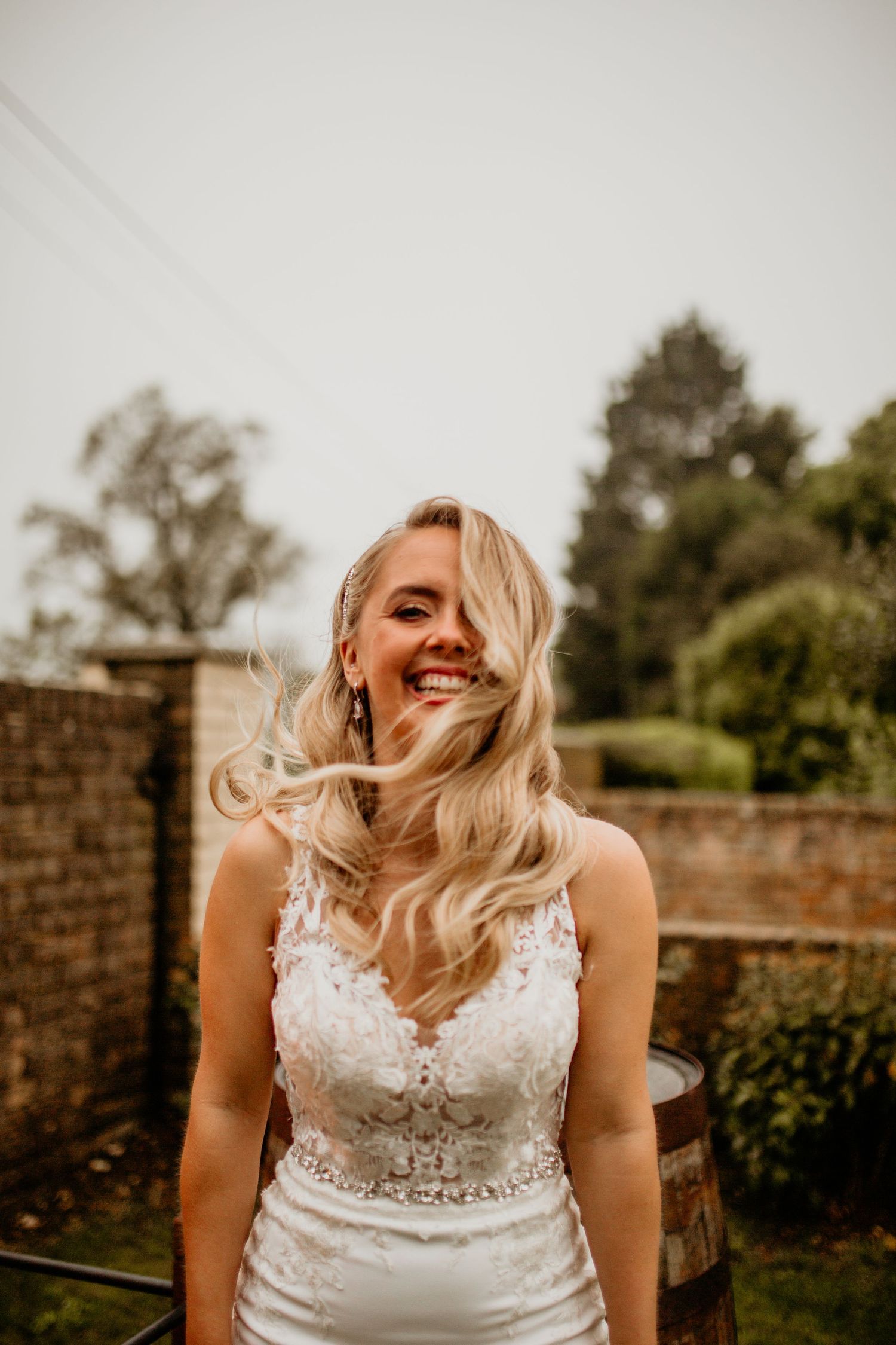 Portrait of a bride in a lace wedding dress with flowing blonde hair against a garden backdrop.