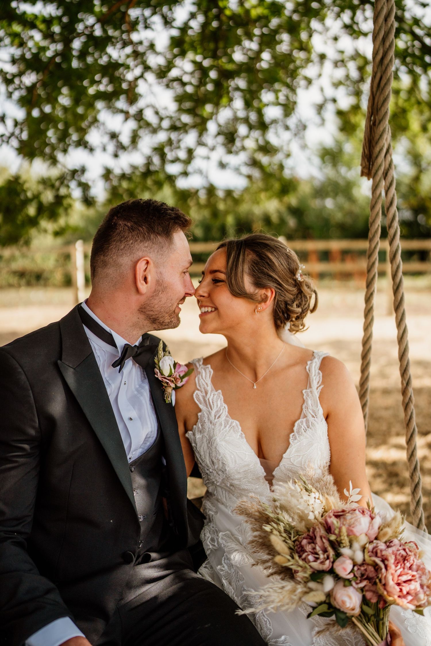 Romantic couple sharing tender moments on decorative rope swing at outdoor wedding venue.