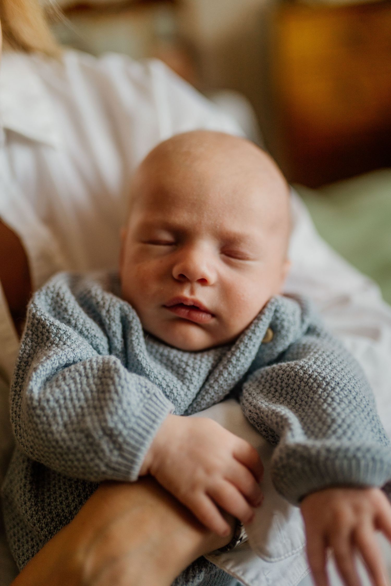 Peaceful sleeping newborn wearing soft gray sweater in gentle natural light.