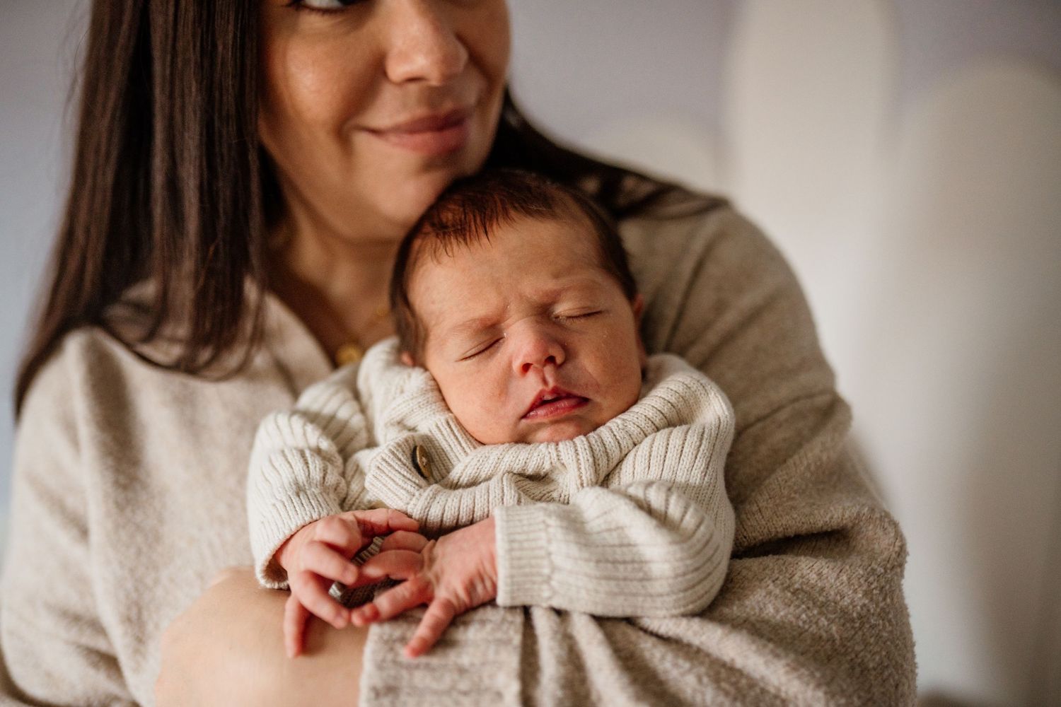 Sweet moment of parent holding sleeping newborn in cozy cream sweater.