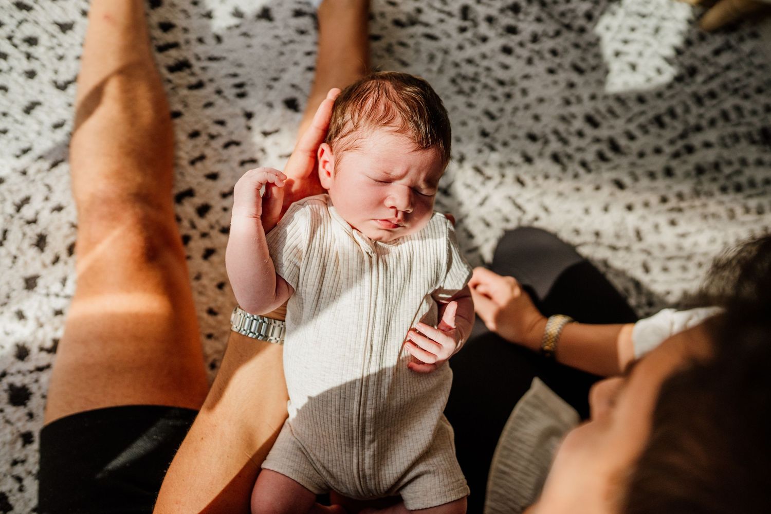Natural lifestyle photography of parents bonding with newborn in living room.