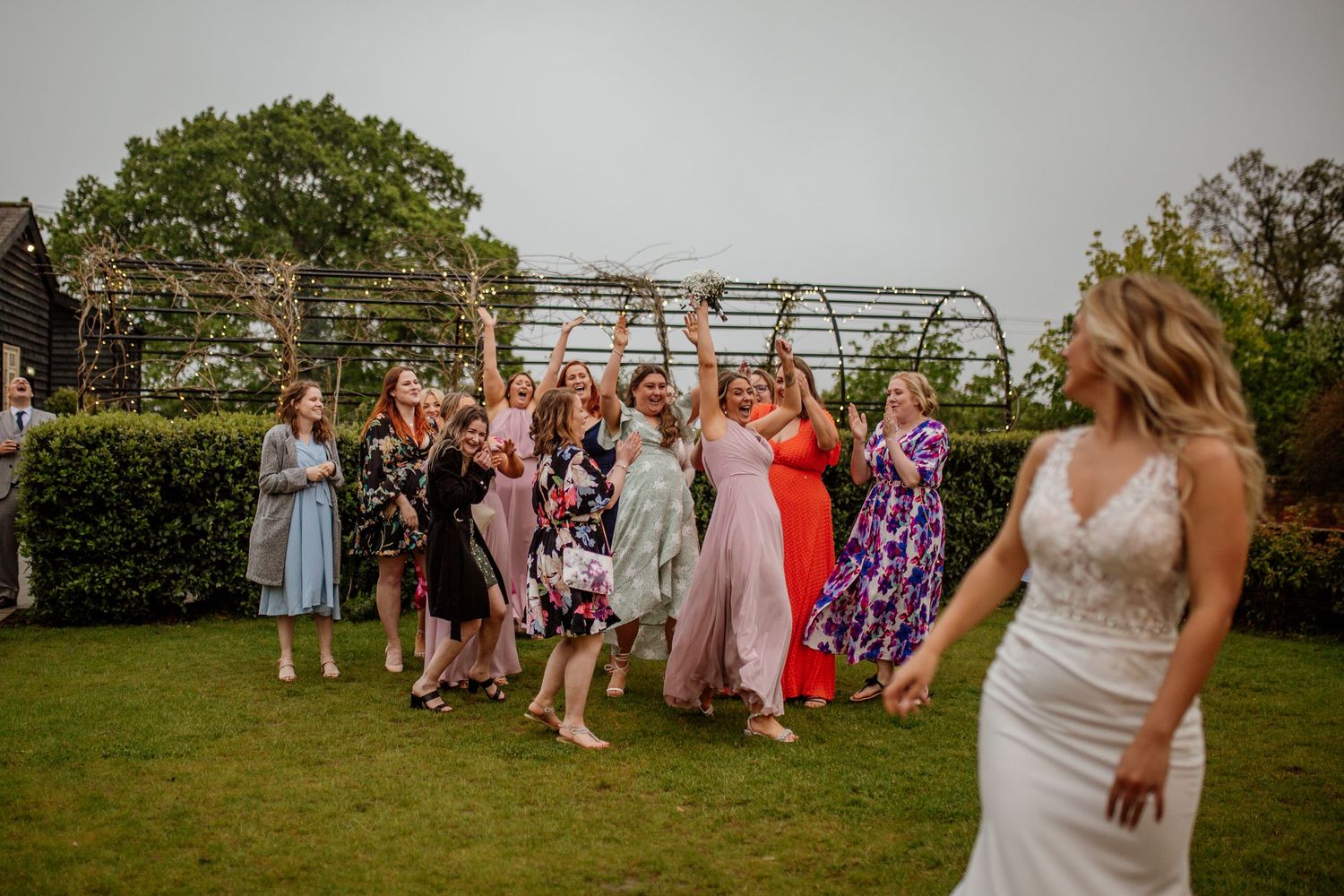 Wedding guests gather on a lawn for the traditional bouquet toss during outdoor reception.