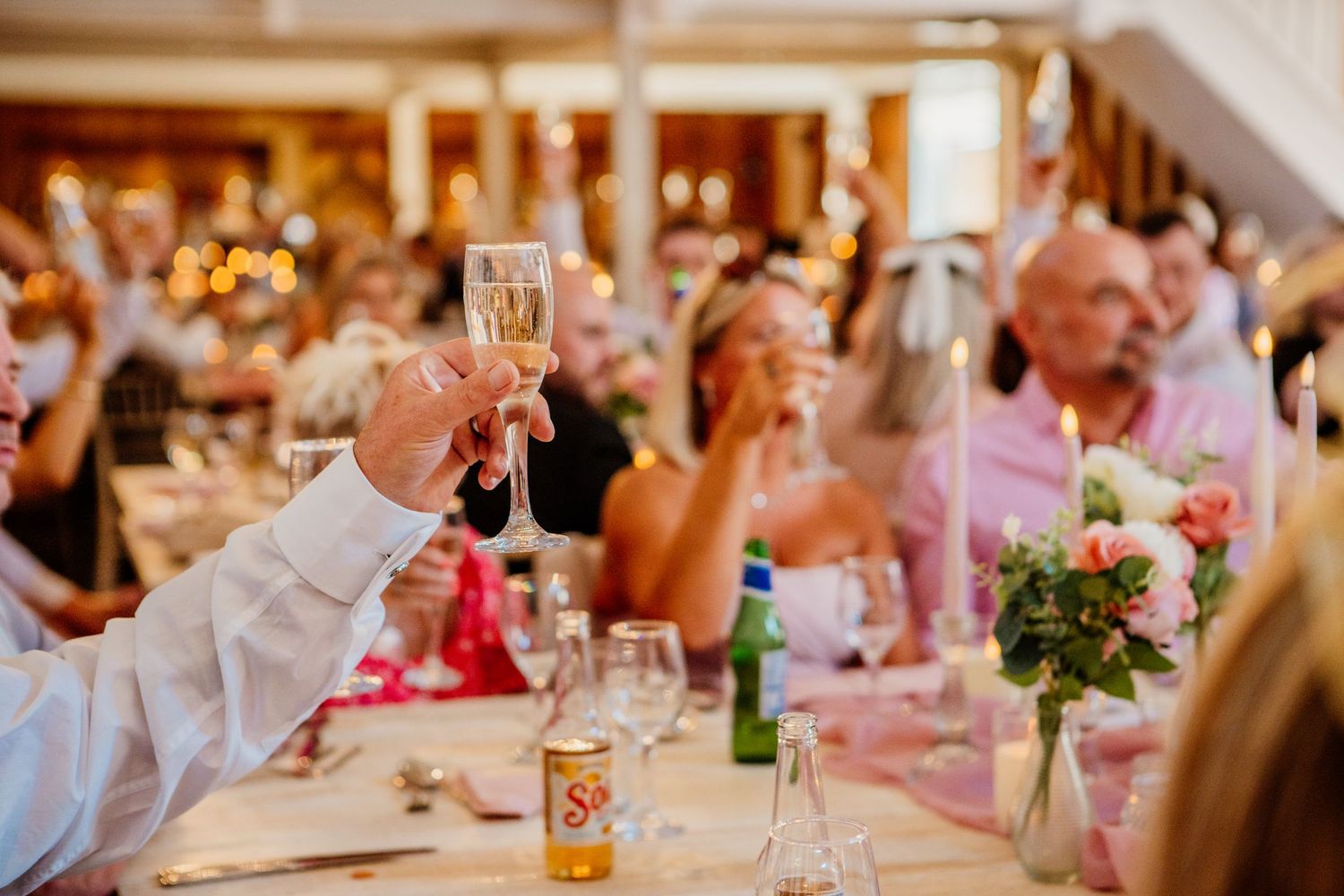 Wedding guests raise their glasses in a toast during an elegant reception dinner celebration.