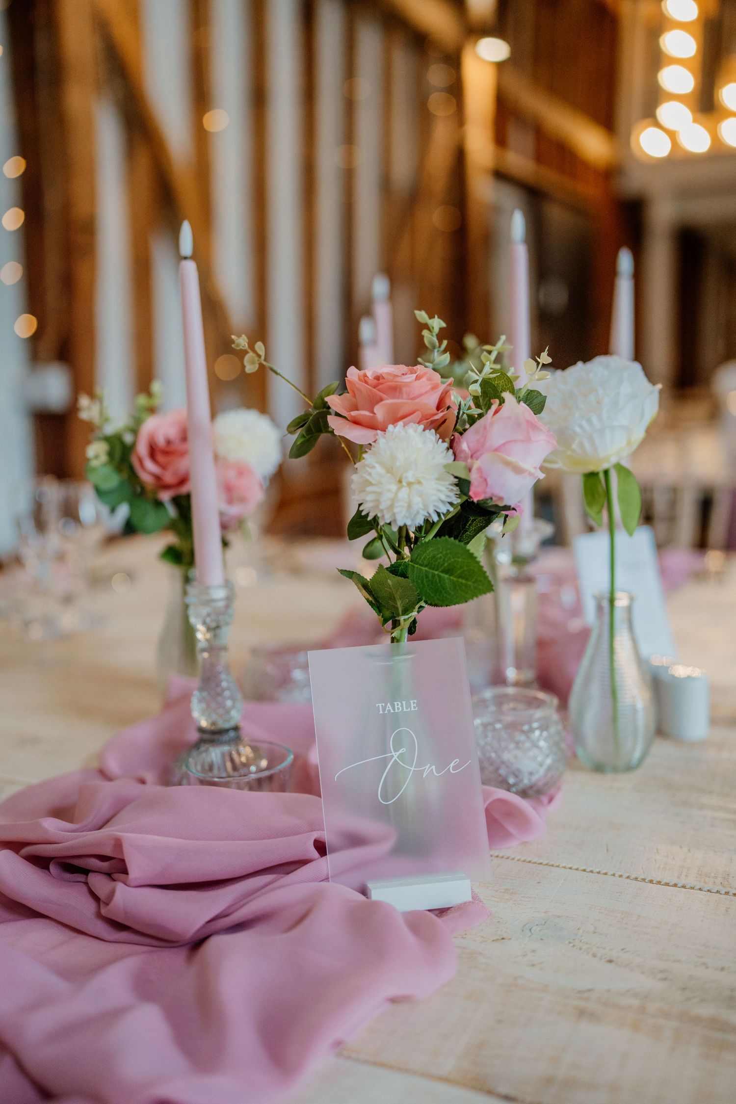 Pink table settings with delicate floral centerpieces and candles create an elegant rustic wedding reception atmosphere.