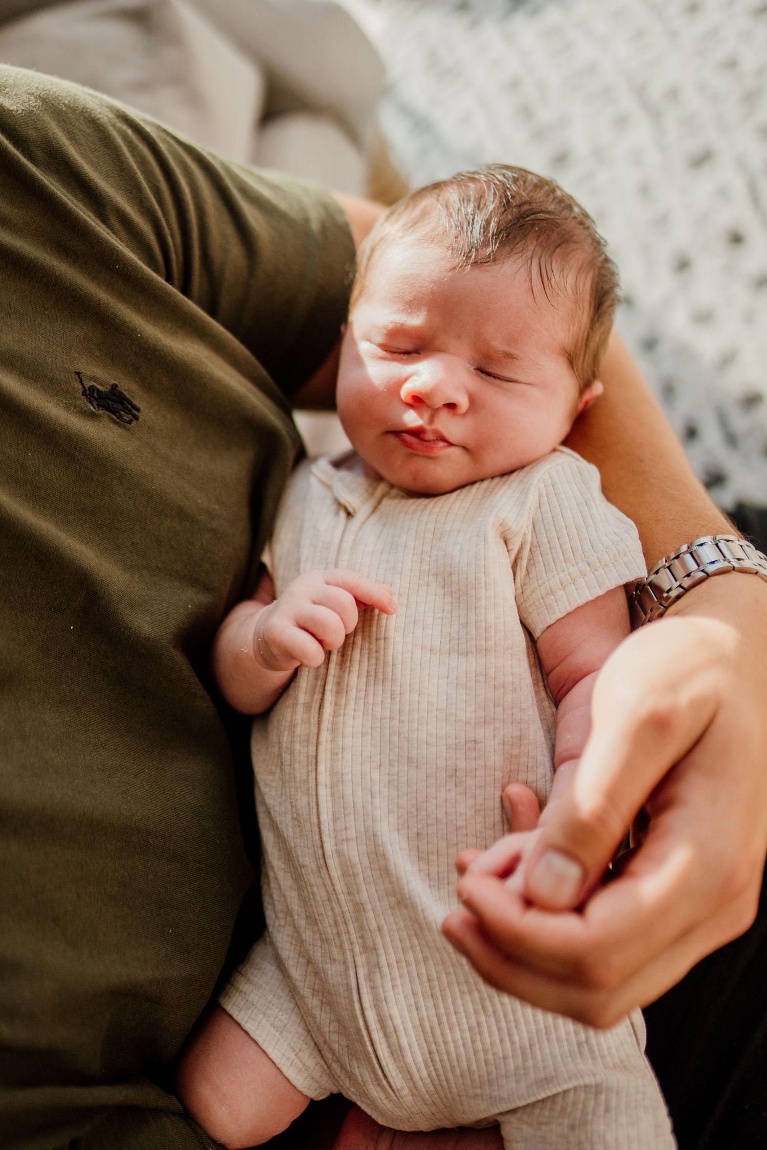 Newborn baby in grey knit onesie sleeping peacefully in caregiver's arms.