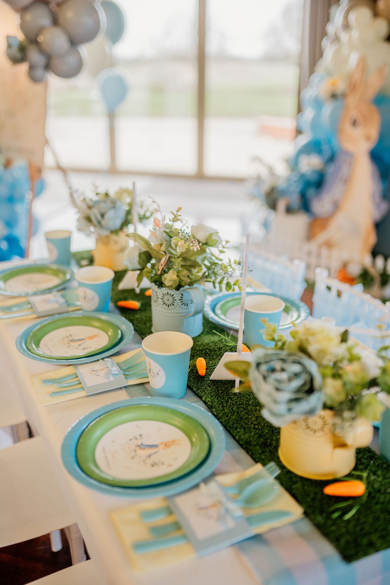 Table settings in blue and white with grass runners and Peter Rabbit themed place settings.