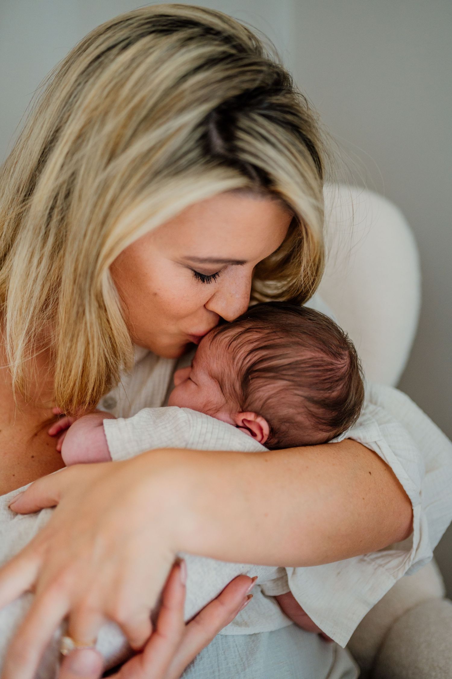 Mother snuggling and bonding with newborn baby on couch in natural light.