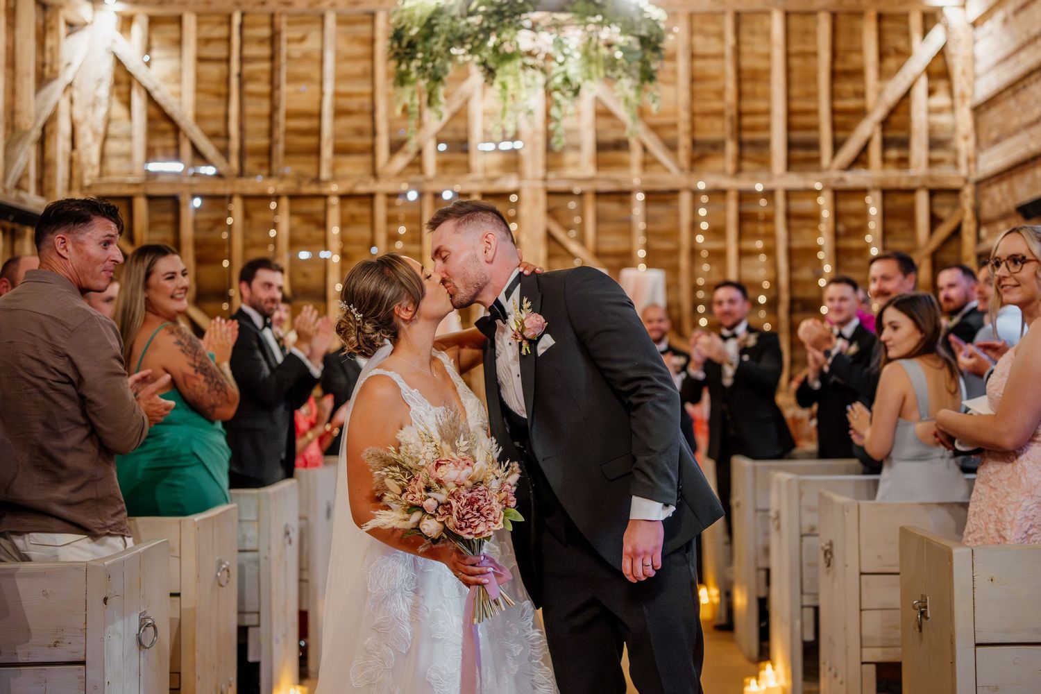Wedding guests dance and celebrate together inside a rustic wooden barn venue during a reception party.