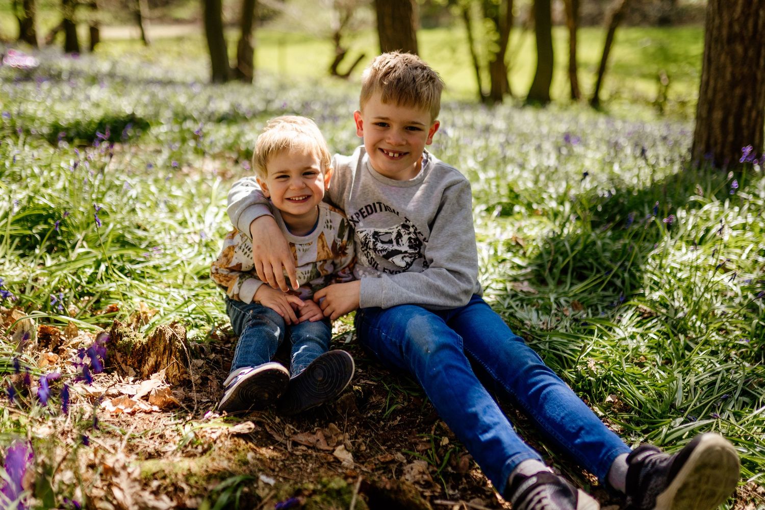 Children playing together in a sunlit forest meadow with white spring flowers blooming on the ground  in Hertfordshire