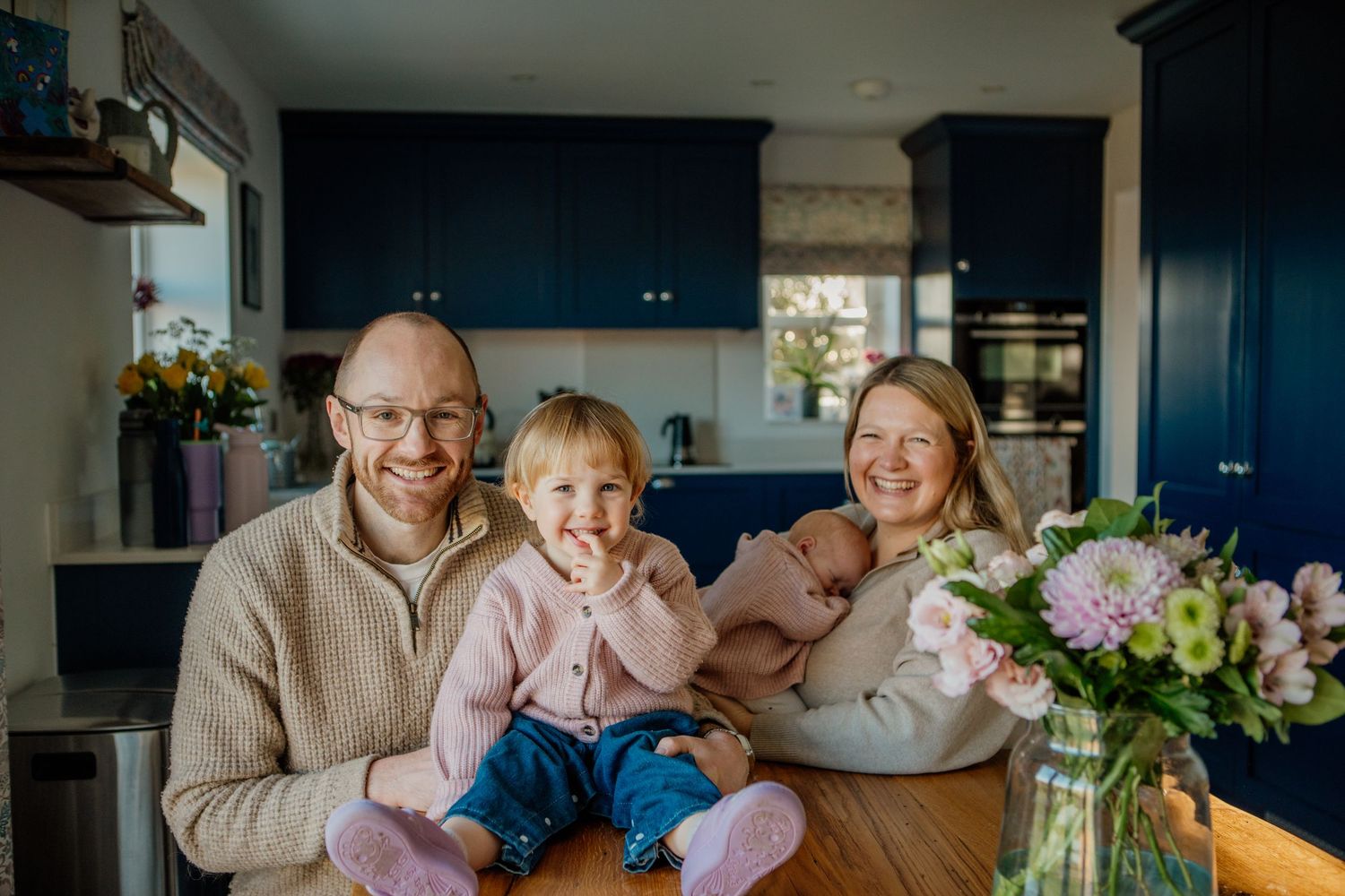 Family sitting together at kitchen counter with blue cabinets and floral arrangement.