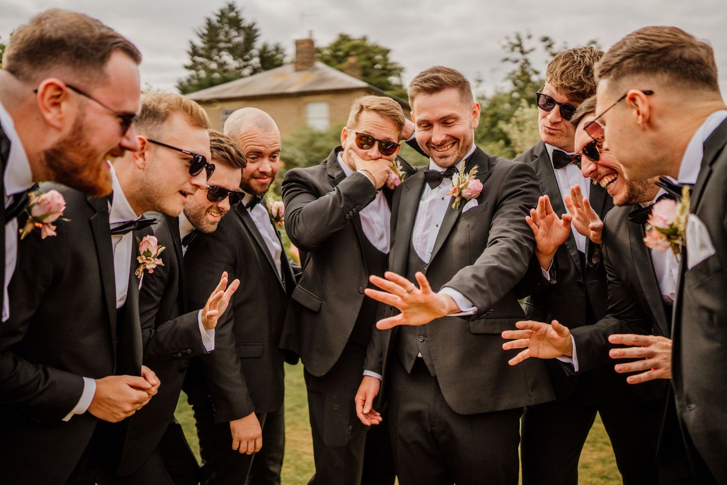 Group of groomsmen in dark suits posing together outdoors.