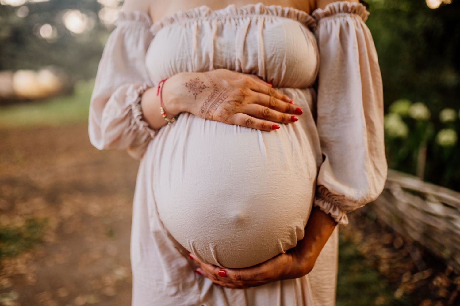 Maternity photo series showing hands cradling a pregnant belly in white dress against natural outdoor backdrop.
