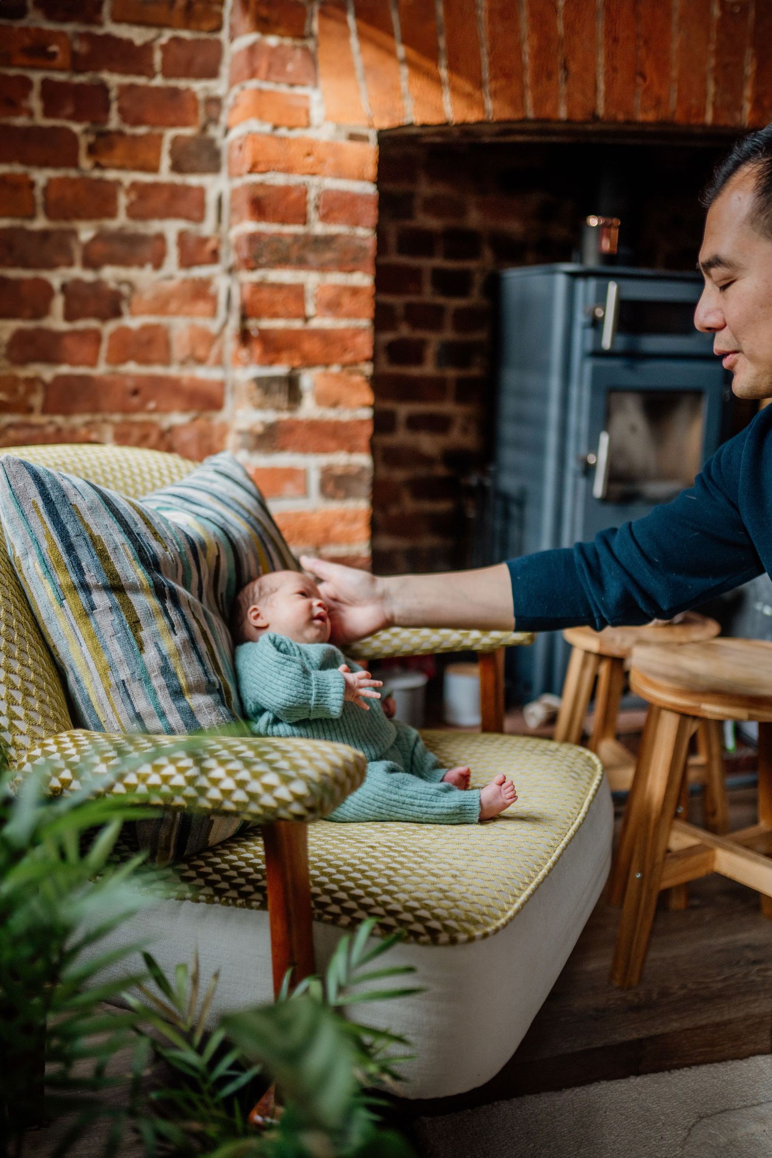 Baby resting on beige couch against exposed brick wall in lifestyle photo series.