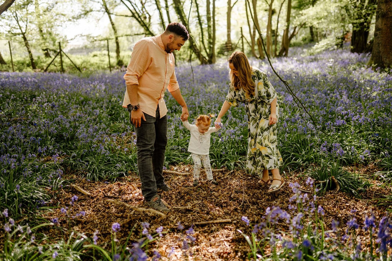 People walk through a serene woodland path filled with blooming bluebells in Hertfordshire on a sunny spring day.