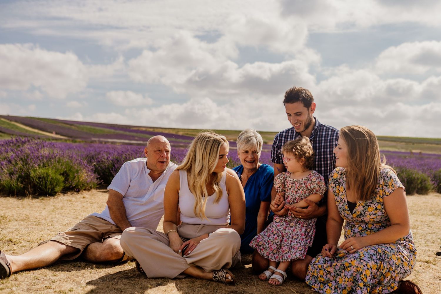 Family group portrait in lavender field, sitting together on sunny day with purple flowers in background.