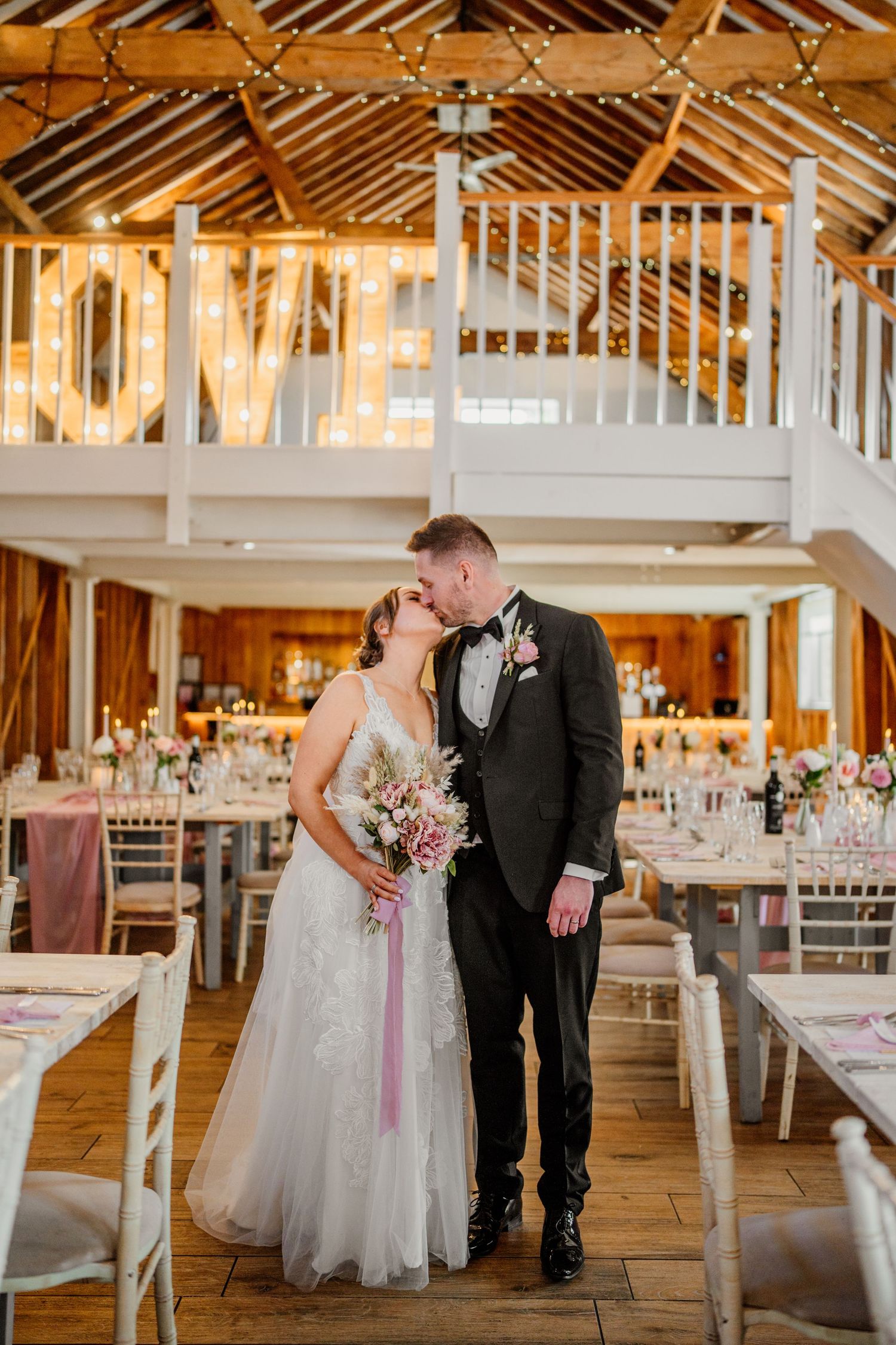 Elegant wedding reception setup in a bright rustic barn venue with white decor and wooden beams.