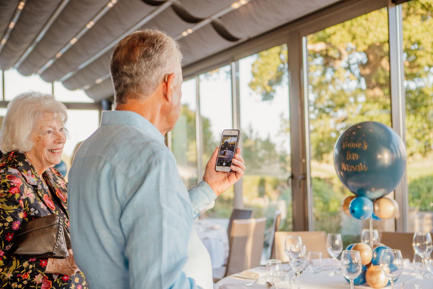 Guests enjoying a sunny outdoor celebration at a venue with large windows.