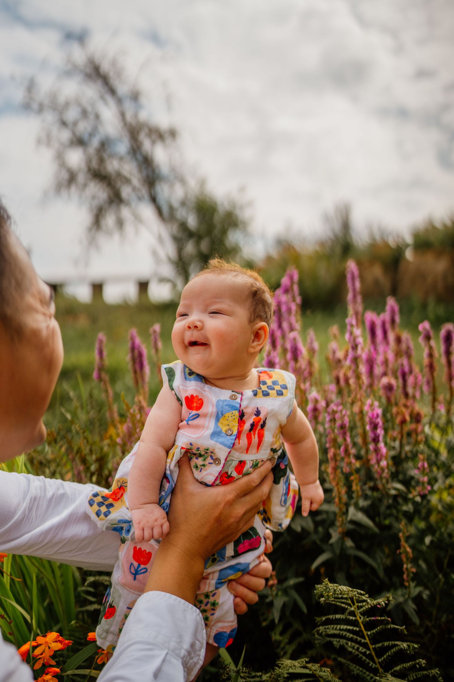 Baby smiling among pink flowers in a garden setting.