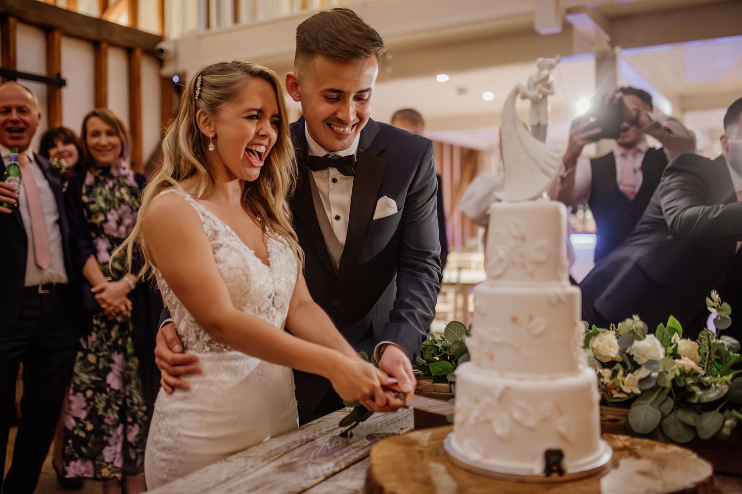 Couple shares a joyful moment while cutting their elegant white wedding cake together.