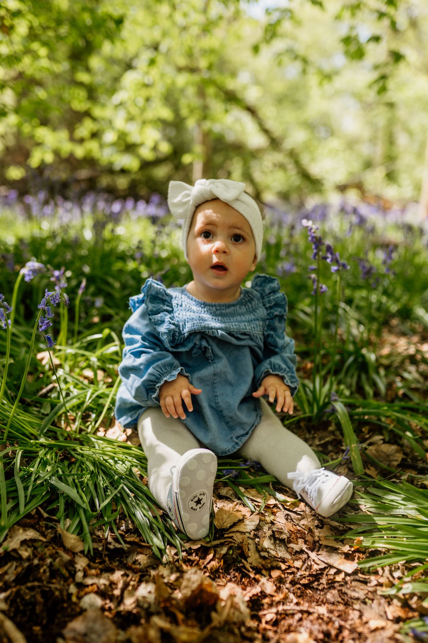 a baby sat amongst bluebells smiling in Hertfordshire