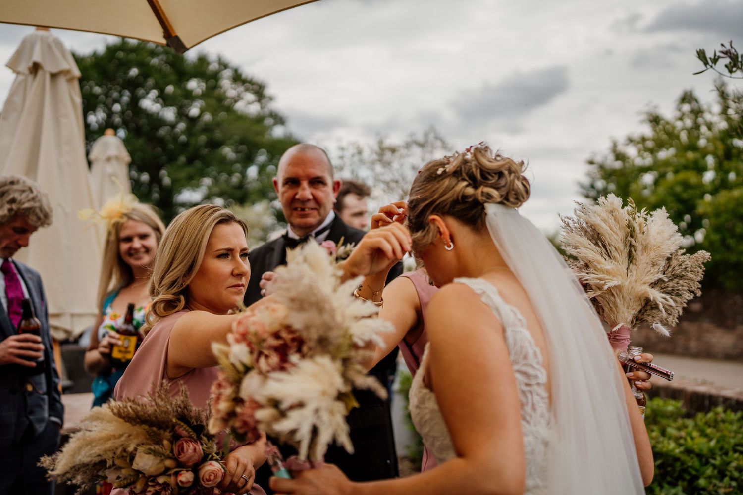 Wedding guests celebrating outdoors on a sunny day with umbrellas and festive atmosphere.