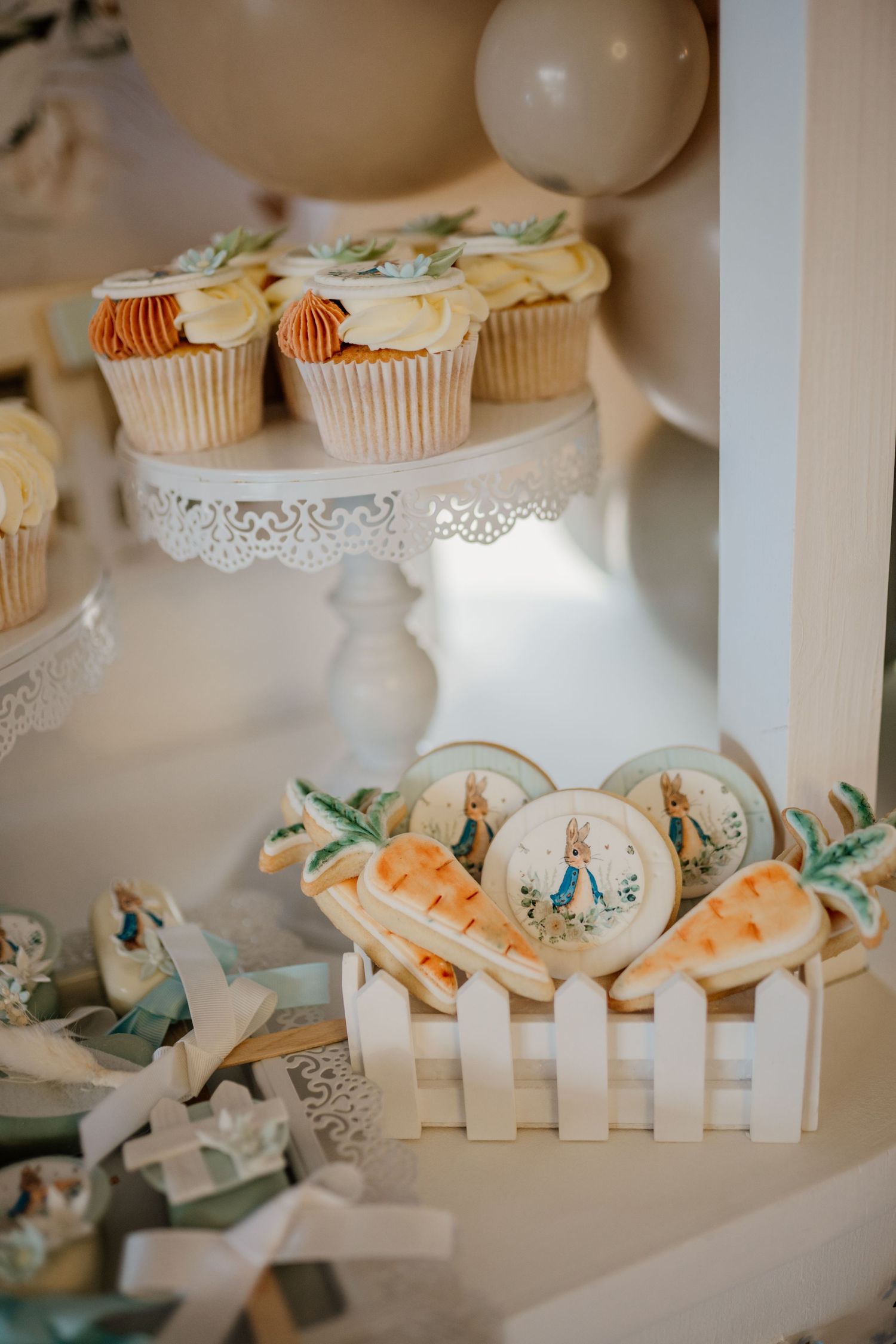 Cupcakes and treats displayed on white picket fence decorations with Peter Rabbit theme elements.