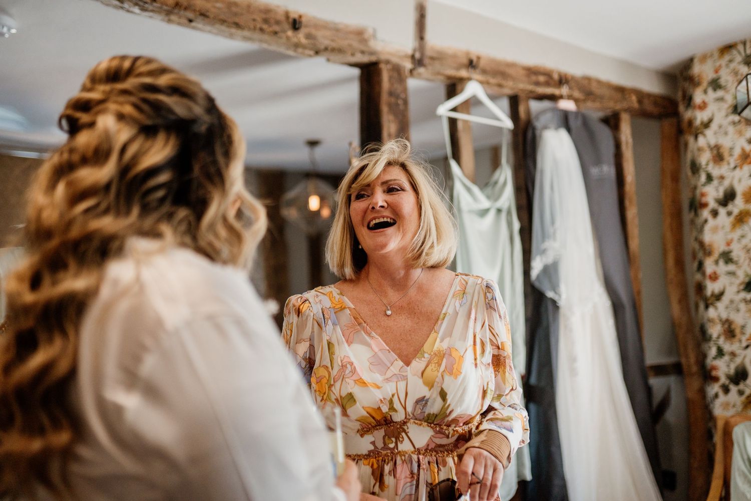 Bridal preparation scene in rustic room with white wedding dress hanging and warm lighting creating joyful atmosphere.