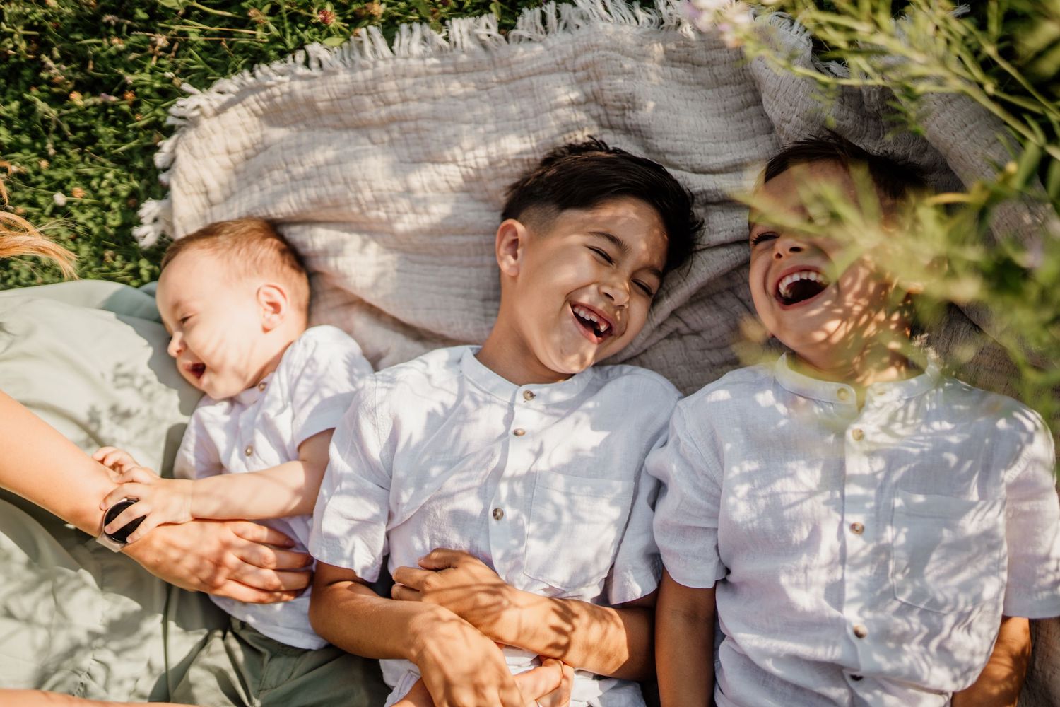 Playful family moment captured under dappled tree shadows.