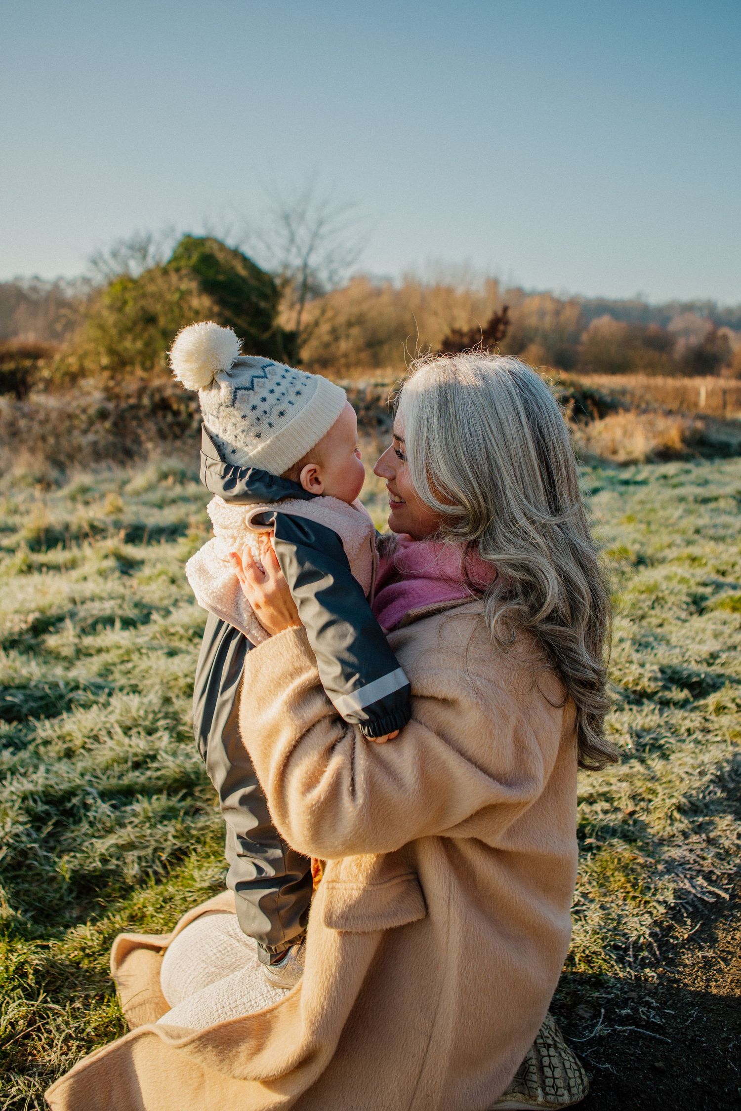 Family embracing outdoors in autumn sunlight wearing warm clothing.