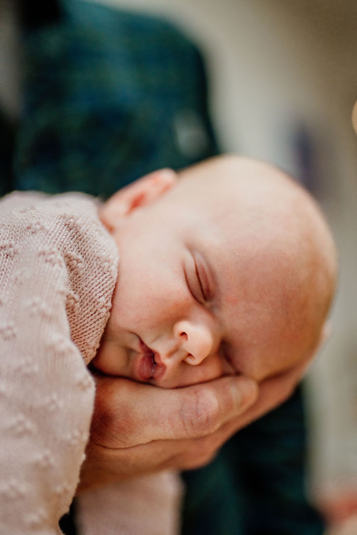 Peaceful closeup of sleeping newborn baby's face resting in gentle hands.