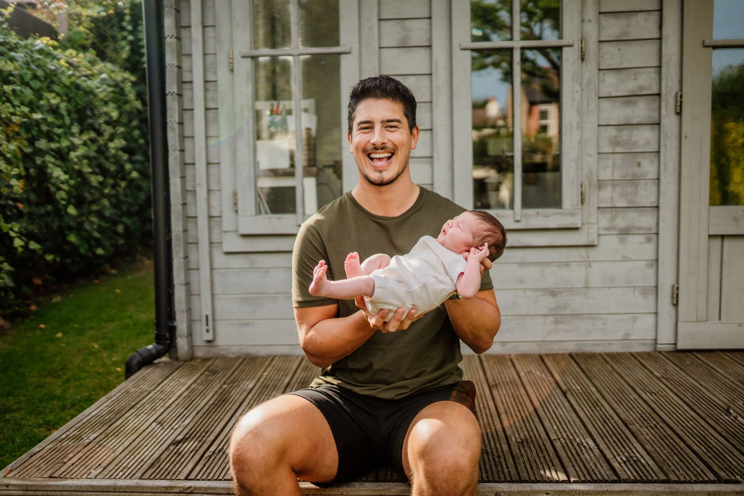 Family photoshoot on wooden deck with rustic house backdrop.