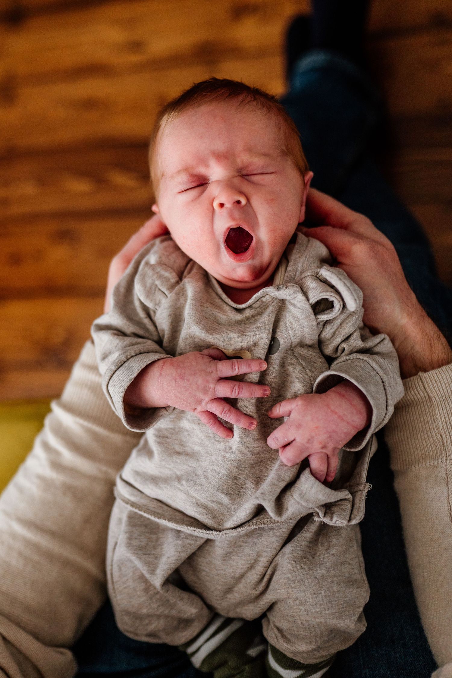 Newborn yawning and stretching in beige outfit during lifestyle photo session.