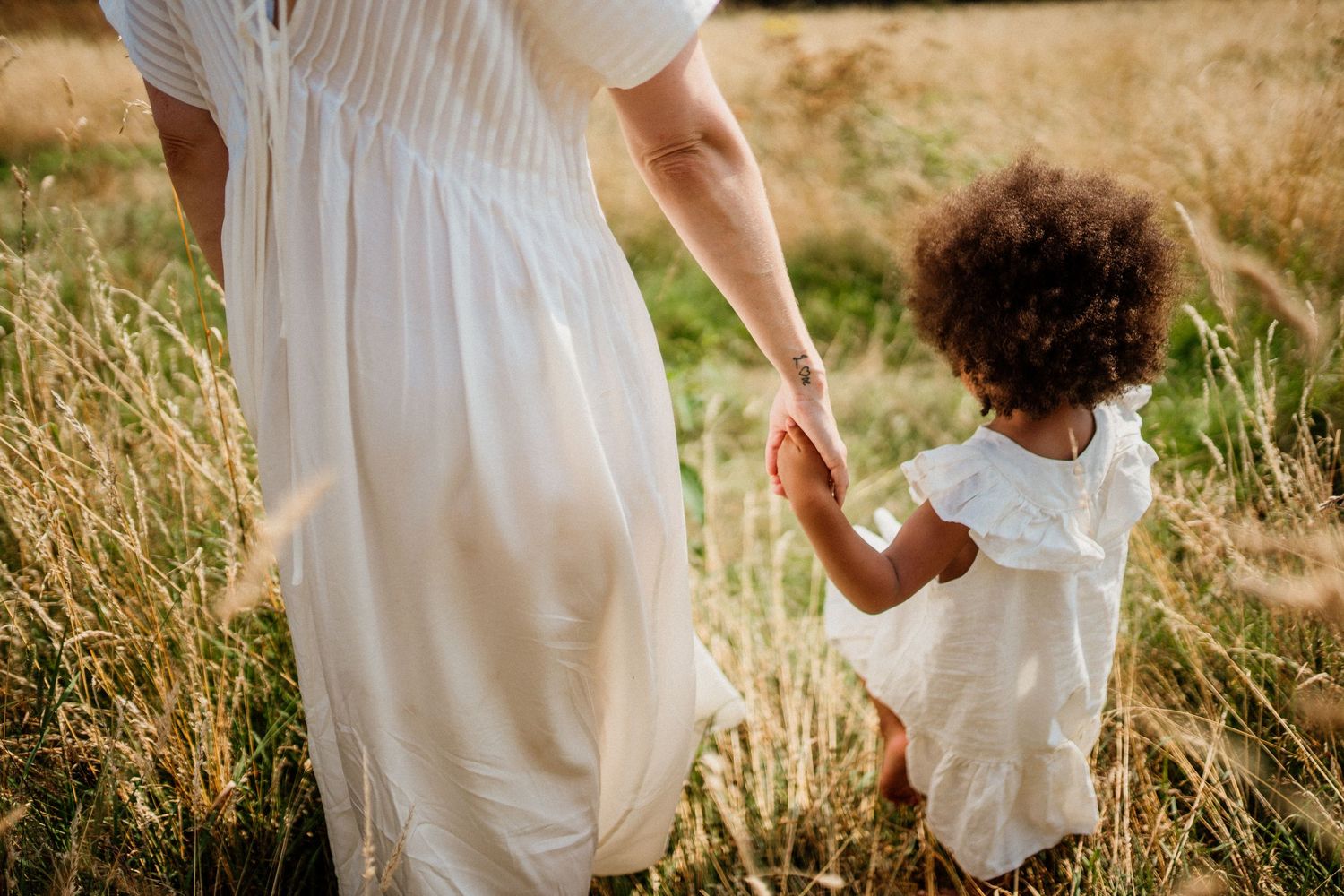 Family members walking hand in hand through summer field in white clothing.