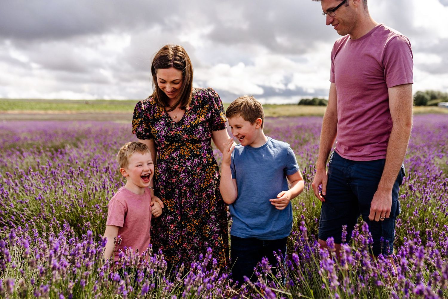Family of four laughing together in a vibrant purple lavender field under cloudy skies.