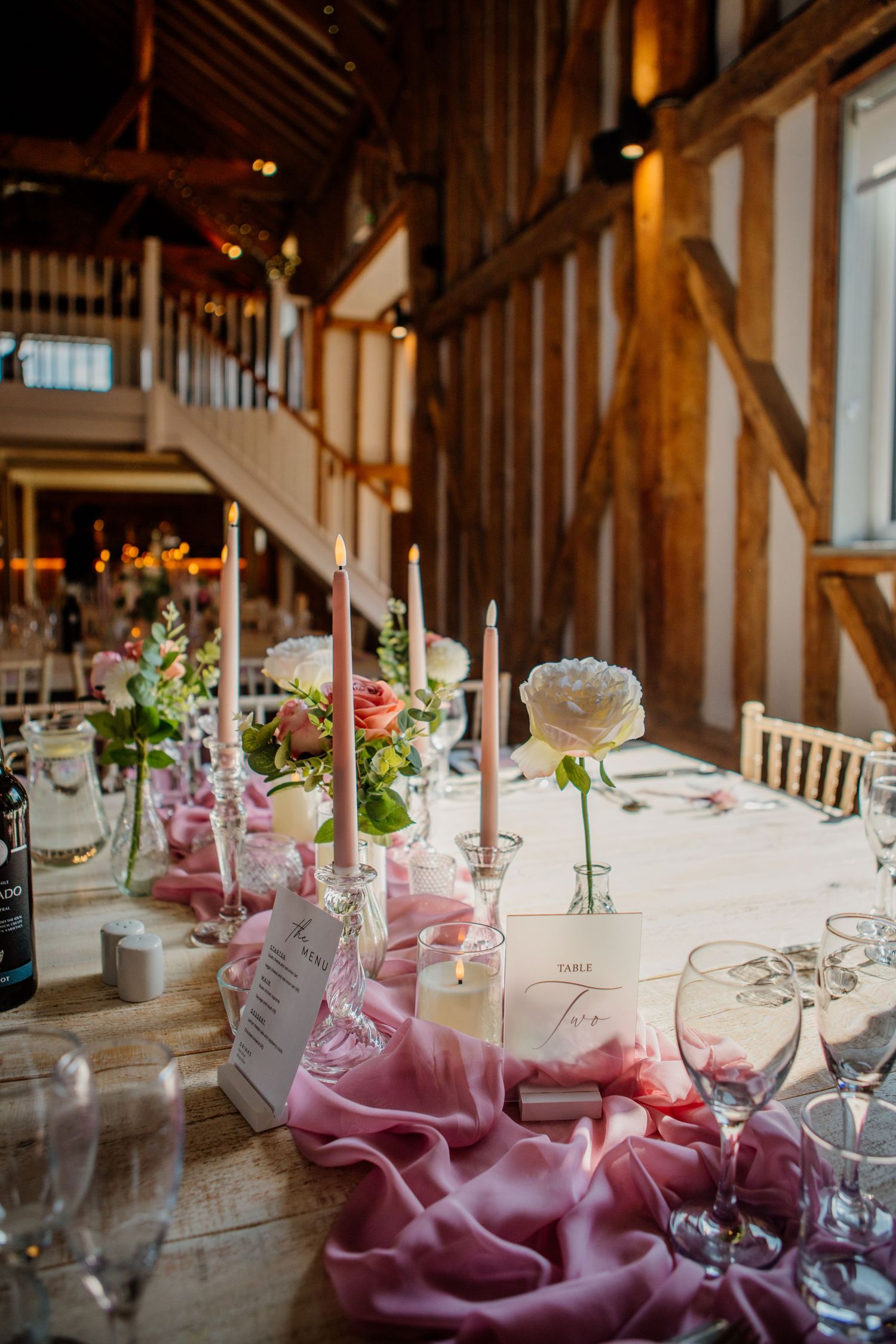 Rustic barn wedding reception tables decorated with pink linens and delicate floral centerpieces.