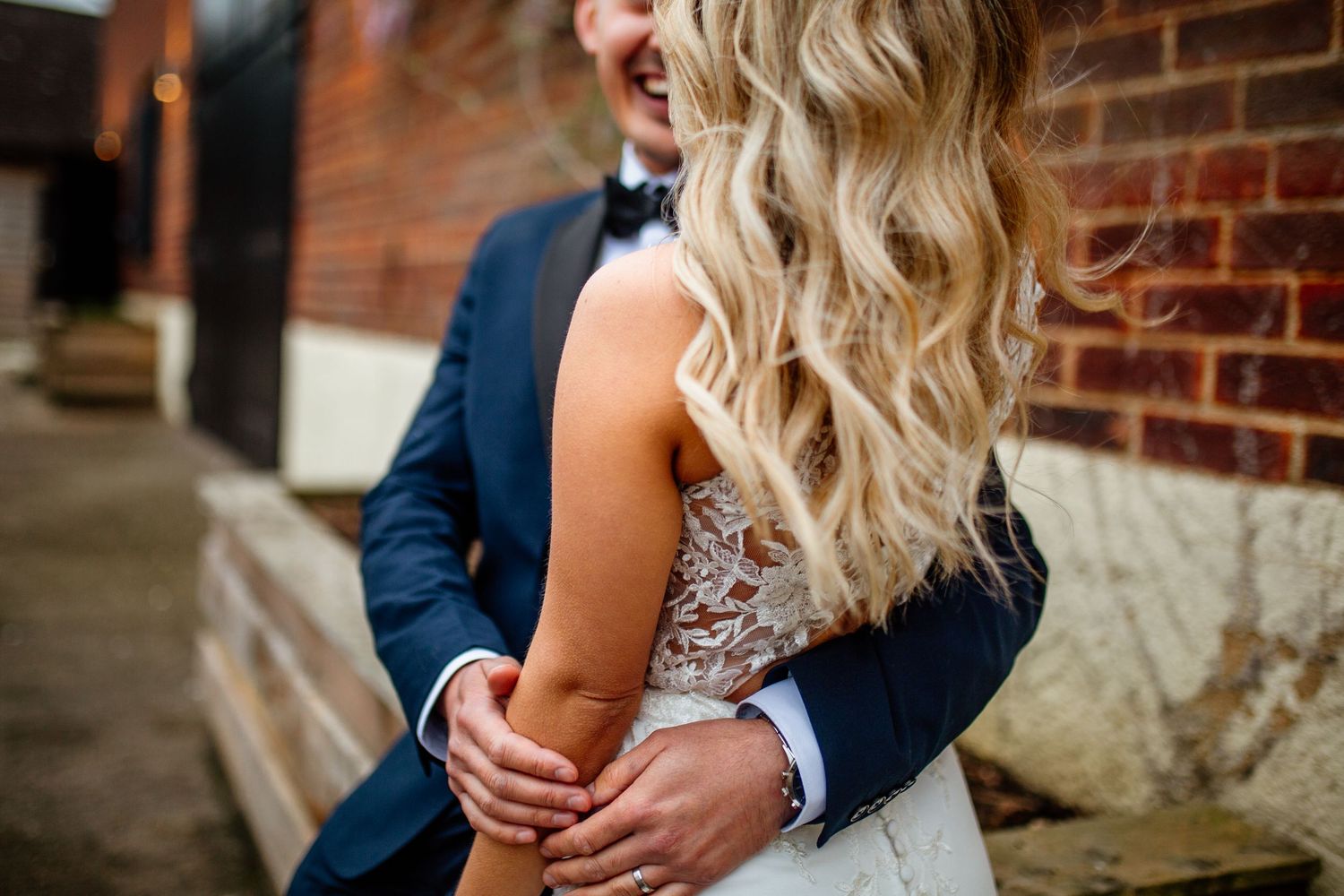 Detail shot of an embrace showing lace wedding dress and navy suit.